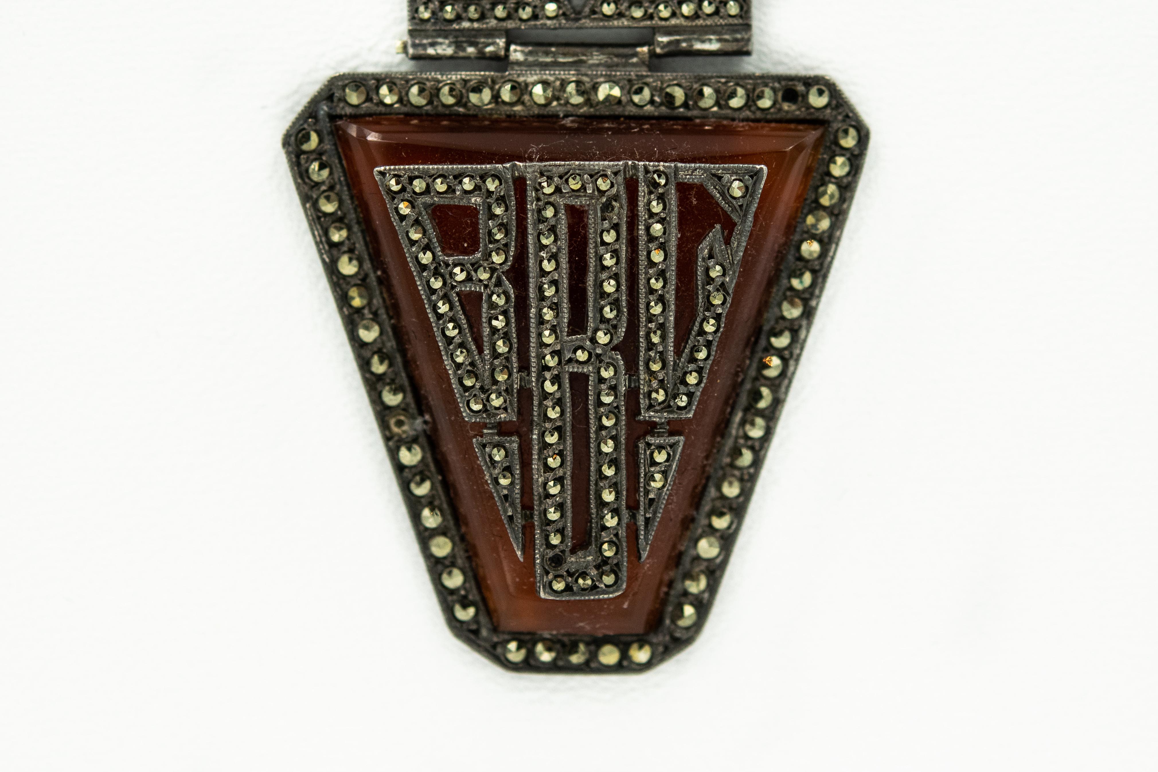 Art Deco lapel brooch pin featuring three sections of marcasite and French carnelian hand cut glass set in white metal. The bottom section features the initials BBC or BRG. . No makers mark, but it is stamped made in France.  The pin area is a