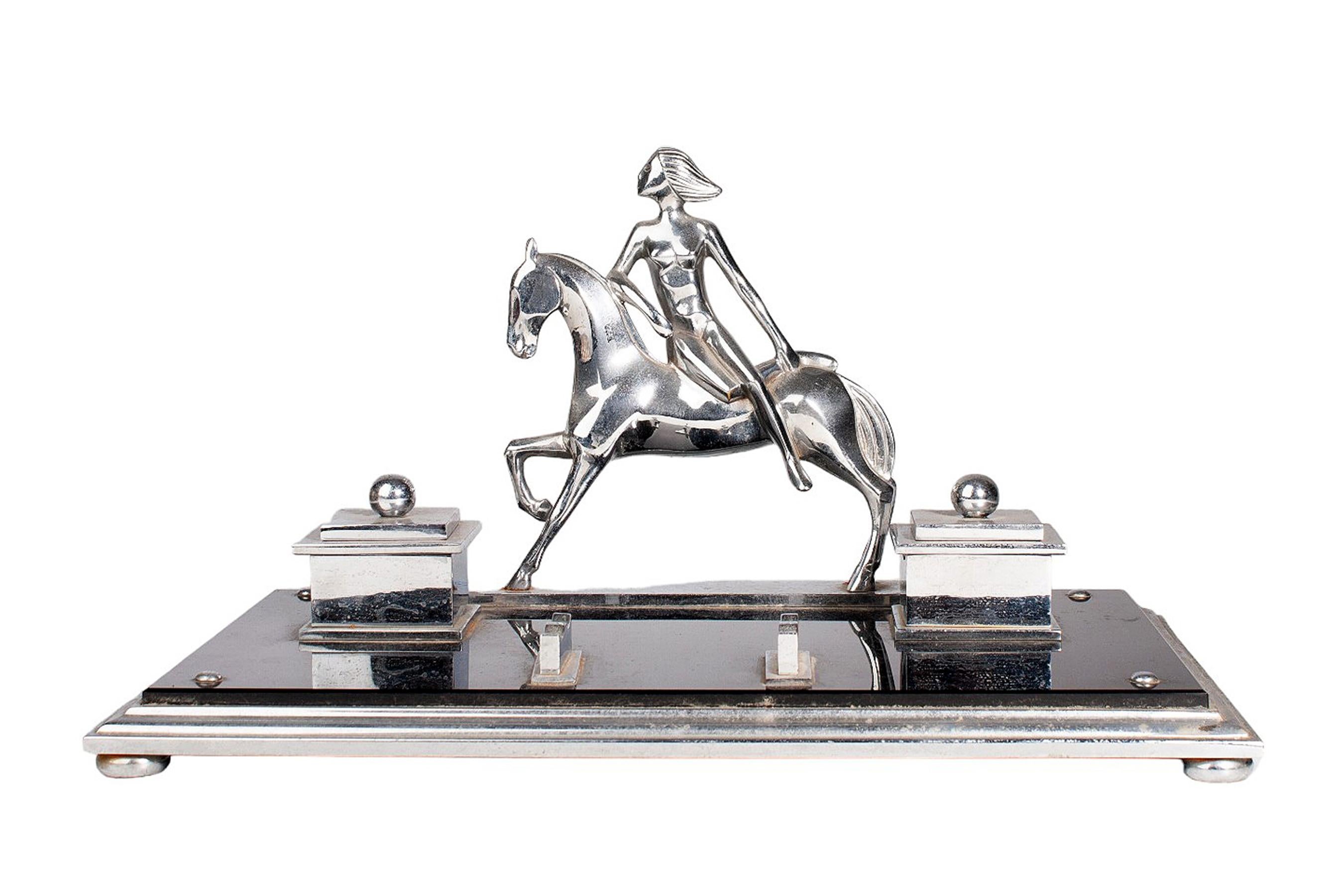 Early 20th century french Art Déco metal desk tidy with woman horseriding, pen holder and a pair of inkwells

By: uknown
Material: metal, silver plate
Technique: cast, molded, polished, metalwork, silvered, plated
Dimensions: 9.5 in x 14.5 in x 8