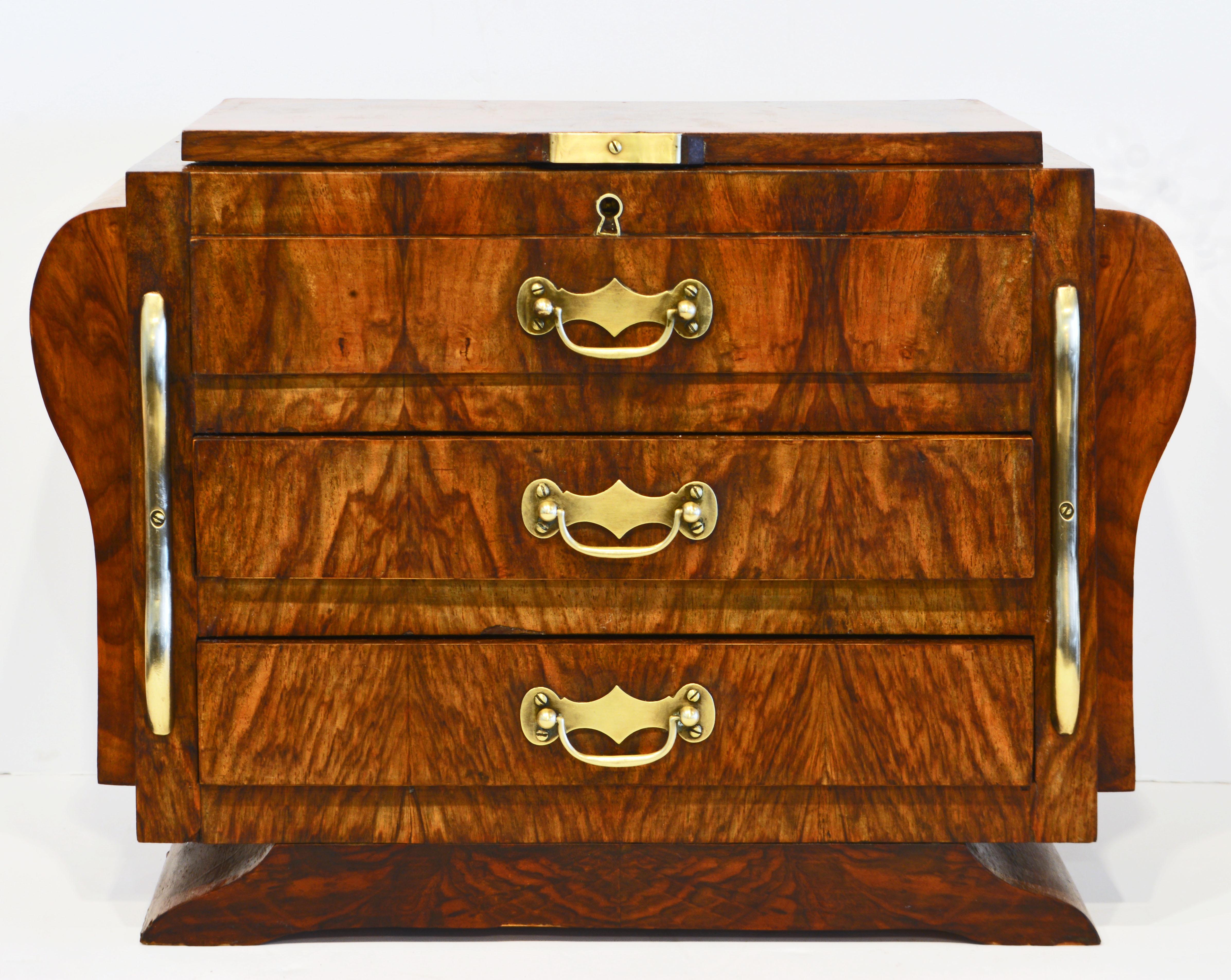 This unusual miniature commode or jewelry box dates to the 1930's and features a top that opens up to a compartment above one simulated and two regular drawers. Flanked by serpentine shape brass mounts. The sides are designed with curved block