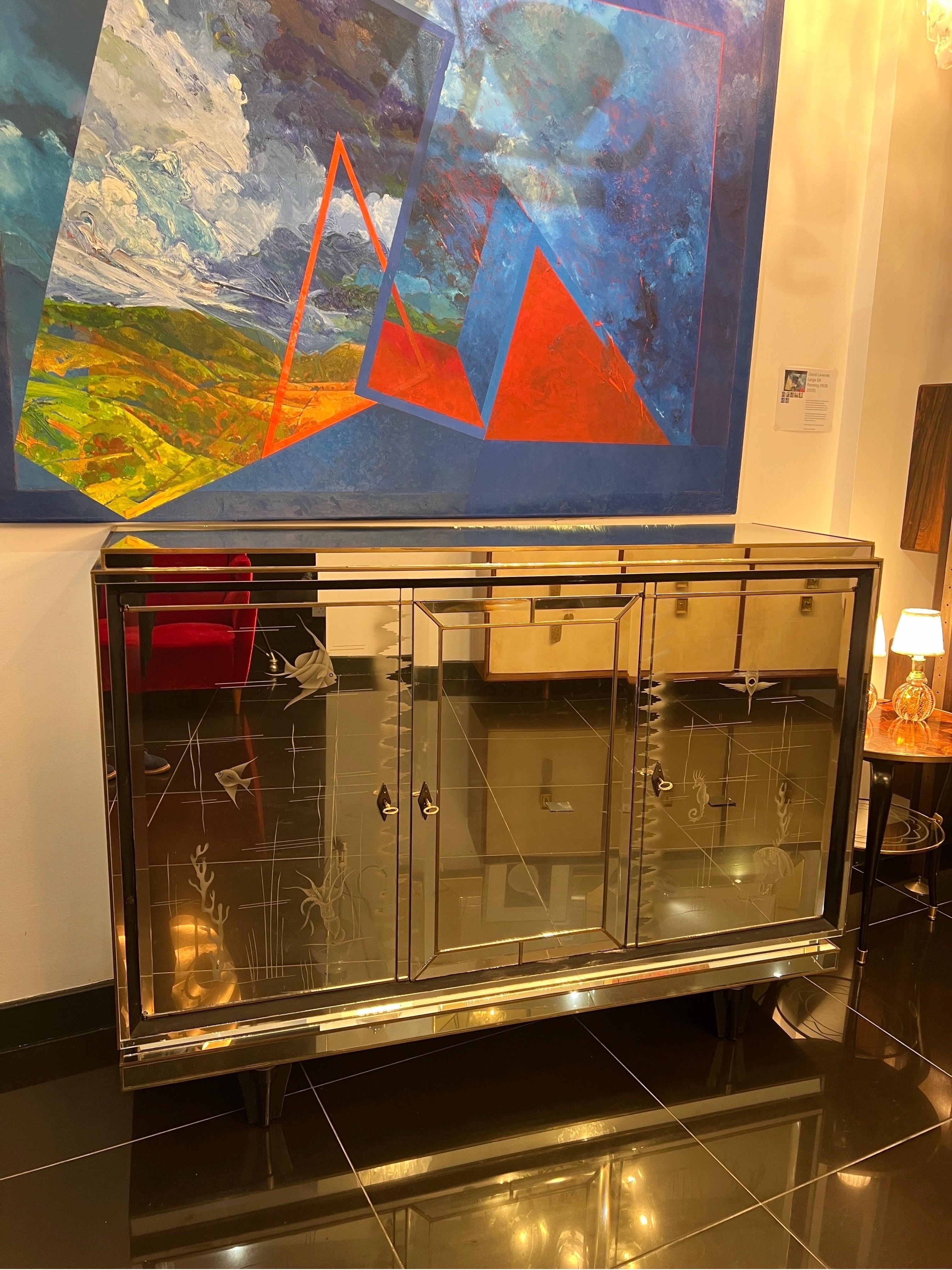 French Art Deco fully mirrored sideboard or a bar cabinet with acquatic designs and brass panelling standing on four black lacquered feet . 
The cabinet consists of three doors, all lockable with brass keys and The inside is incased in wood with two
