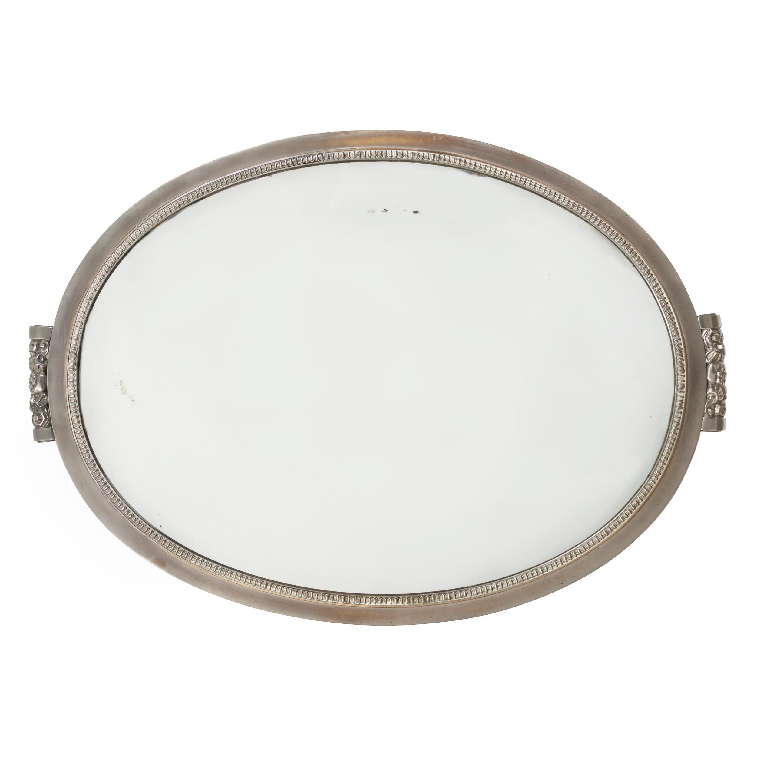 A superb Art Deco wall mirror, it features a nickel-plated steel frame surrounding an ovular mirrored glass with cast steel floral motifs affixed top and bottom with machined screws. It is designed to be hung either vertically or