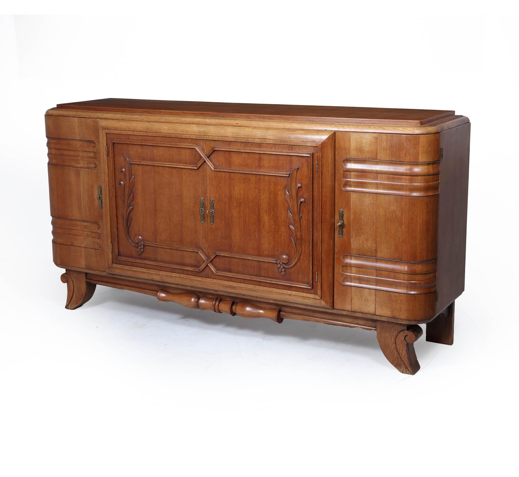 Art Deco Oak Sideboard 
A large and bold French Art Deco sideboard in solid oak, circa 1930s. The design combines a sculptural quality with traditional craftsmanship—featuring deep carved relief to the central doors, fluted rounded ends, and a