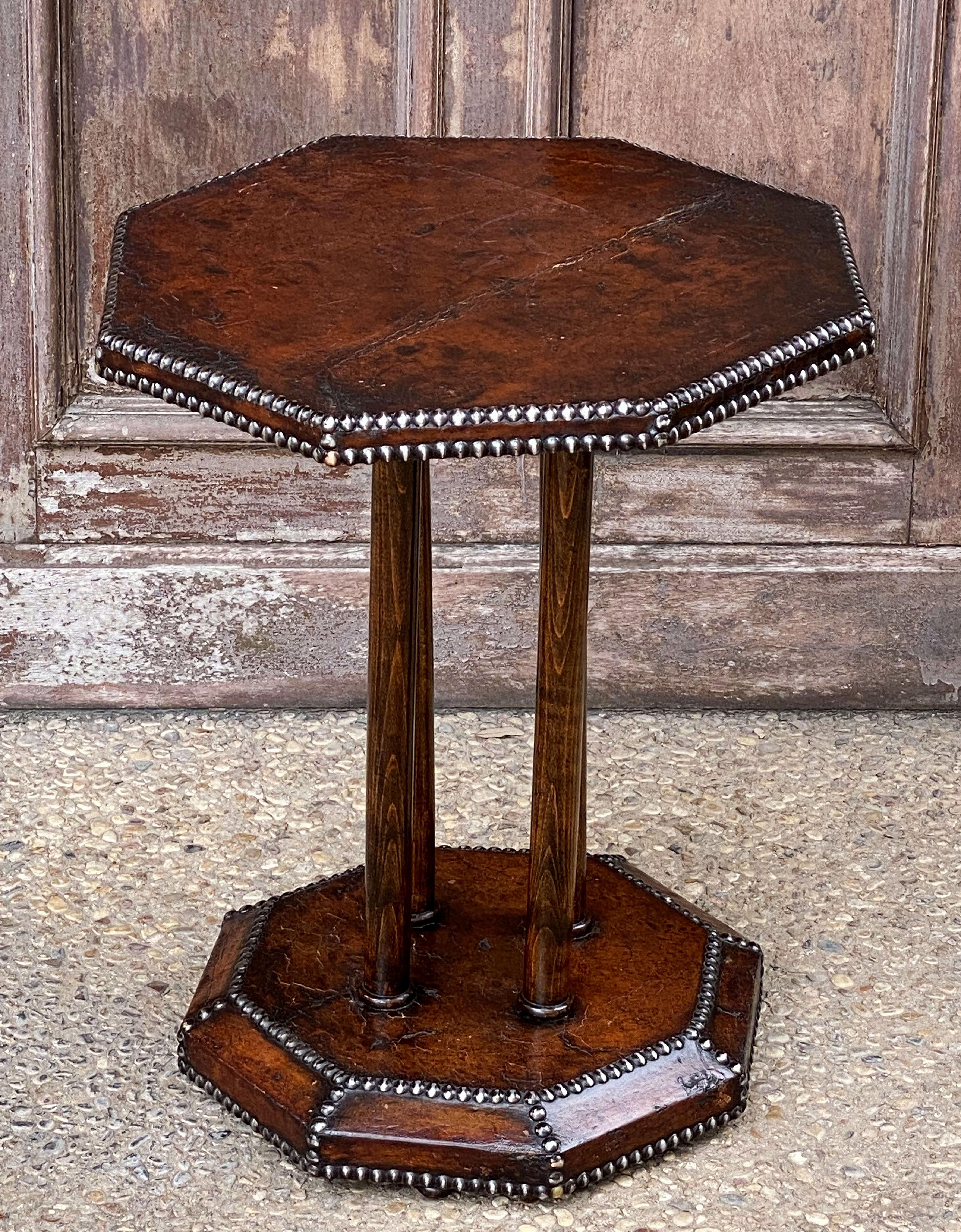 A fine French octagonal top occasional or bistro table from the Art Deco era, featuring a leather-wrapped top with brass nail-head detail, over four wood pedestal supports mounted to a smaller octagonal base also covered in a studded leather,