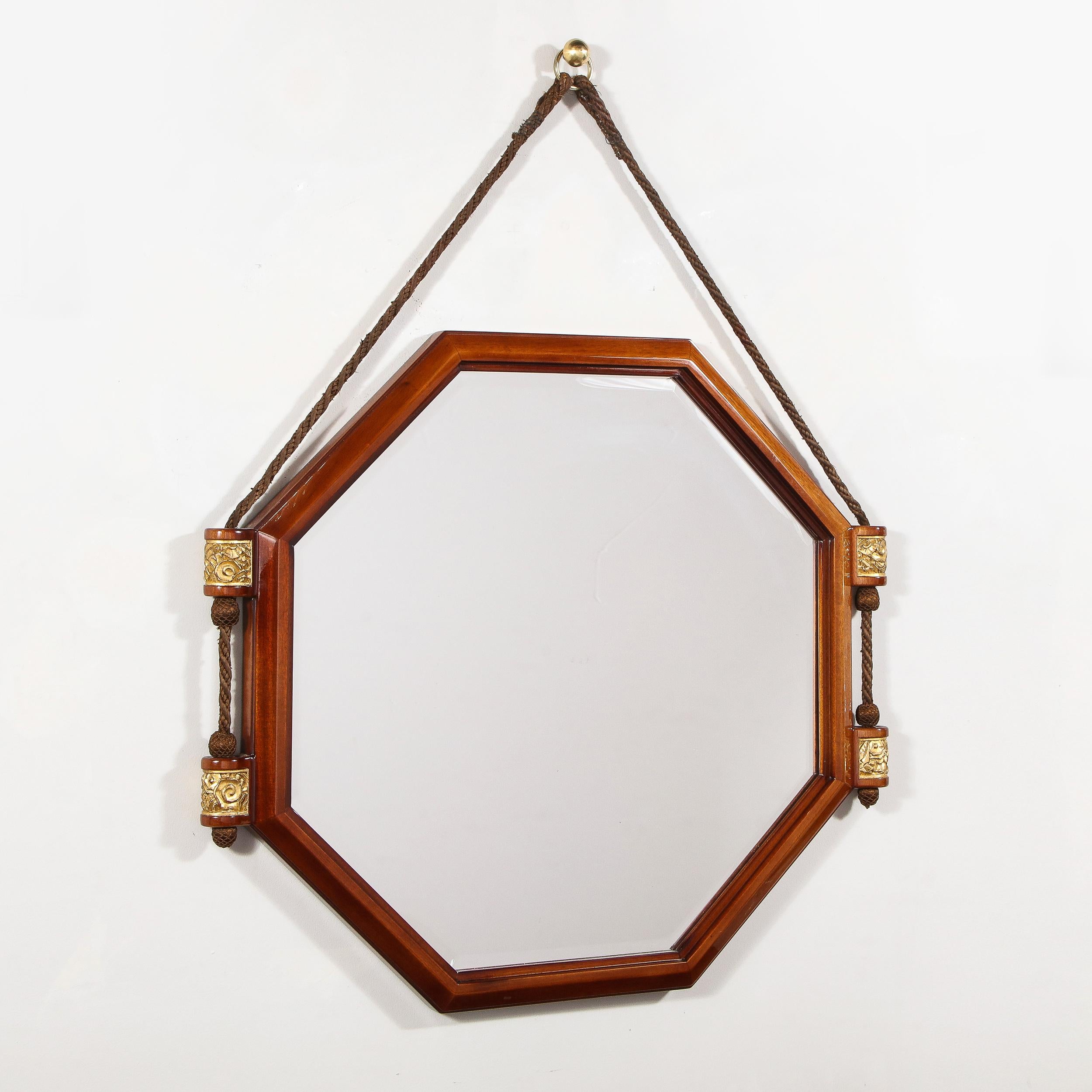 This stunning Art Deco mirror mirror was realized in France circa 1930. It features an octagonal form in walnut wiht a plain beveled mirror in the center. The mirror hangs from a java hued cotton cord that attaches to two cylindrical walnut supports
