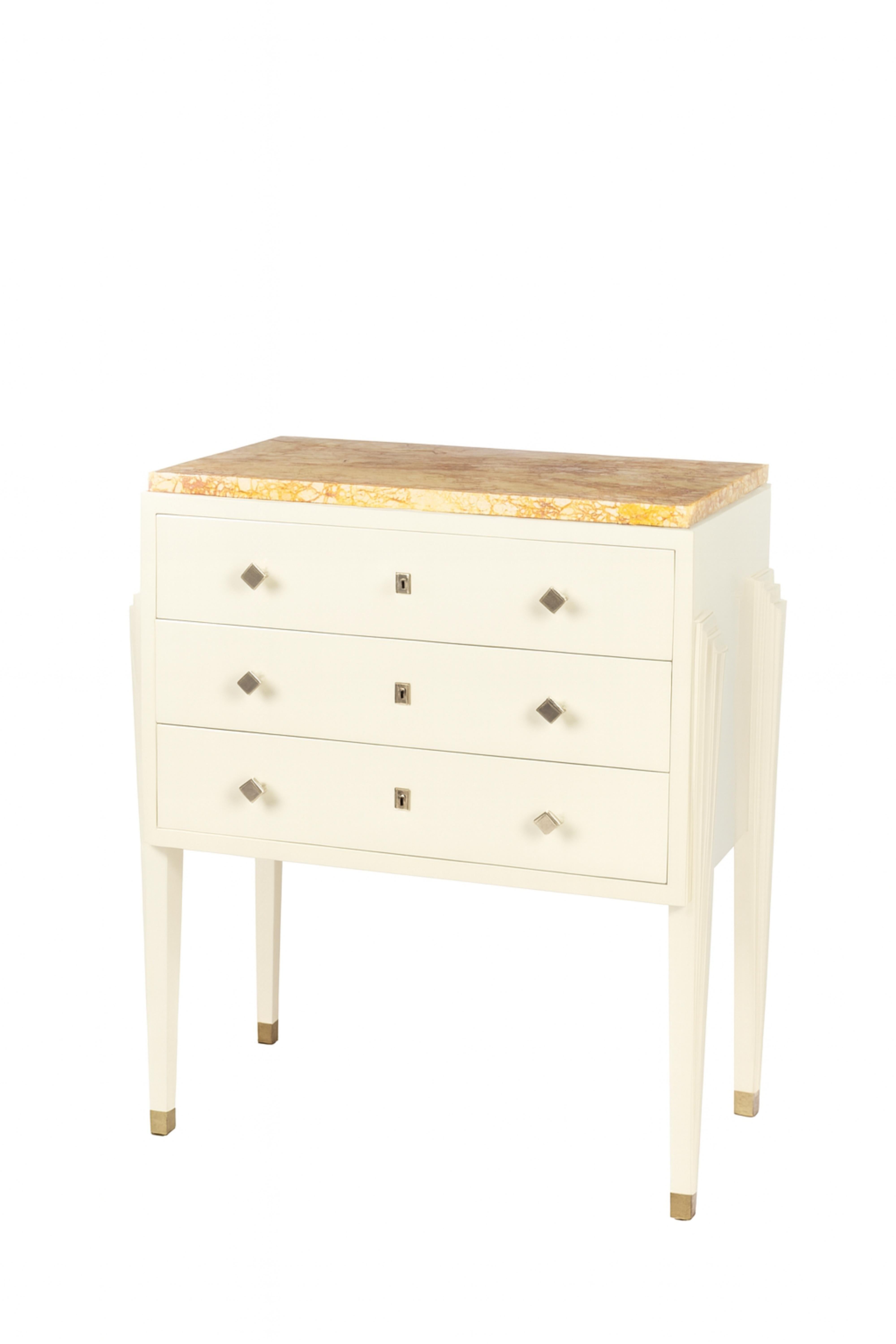 A  three-drawer commode featuring a sleek off white (color reference: #F2F0EF) lacquer high-gloss finish lacquered finish complemented by elegant chrome hardware. This sophisticated piece is crafted from rare red Verona marble, quarried in Verona,