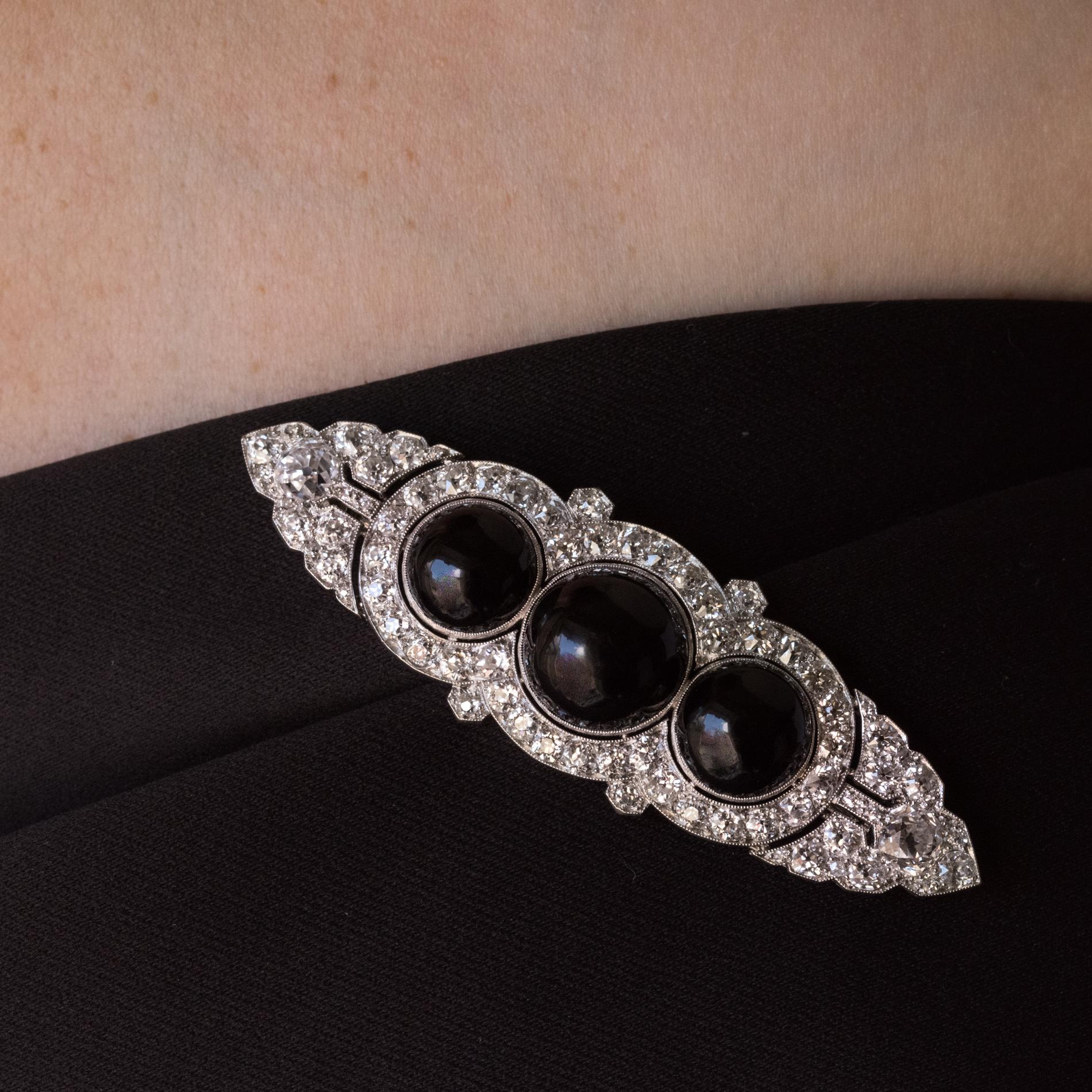Brooch in platinum and 18 carat, white gold.

Adorned with 3 onyx cabochons in an openwork bezel setting surrounded by antique cut diamonds. 

Principal Onyx: diameter 12.5 mm, side 2: diameter 9.8 mm.
Total weight of diamonds: 4.40 carat