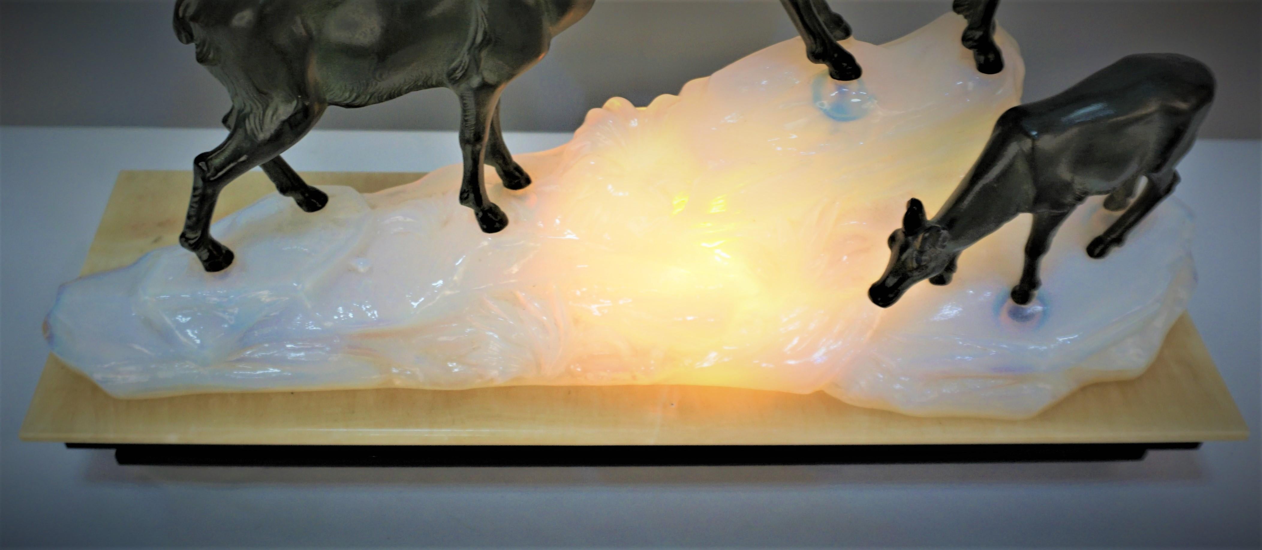 Beautiful Art Deco sculpture lamp, Beige onyx sitting on black marble as base, golden blue opaline glass rocky mountain with light inside and standing antelopes on the top of the rock (metal sculptures might have been commissioned or done by Max le