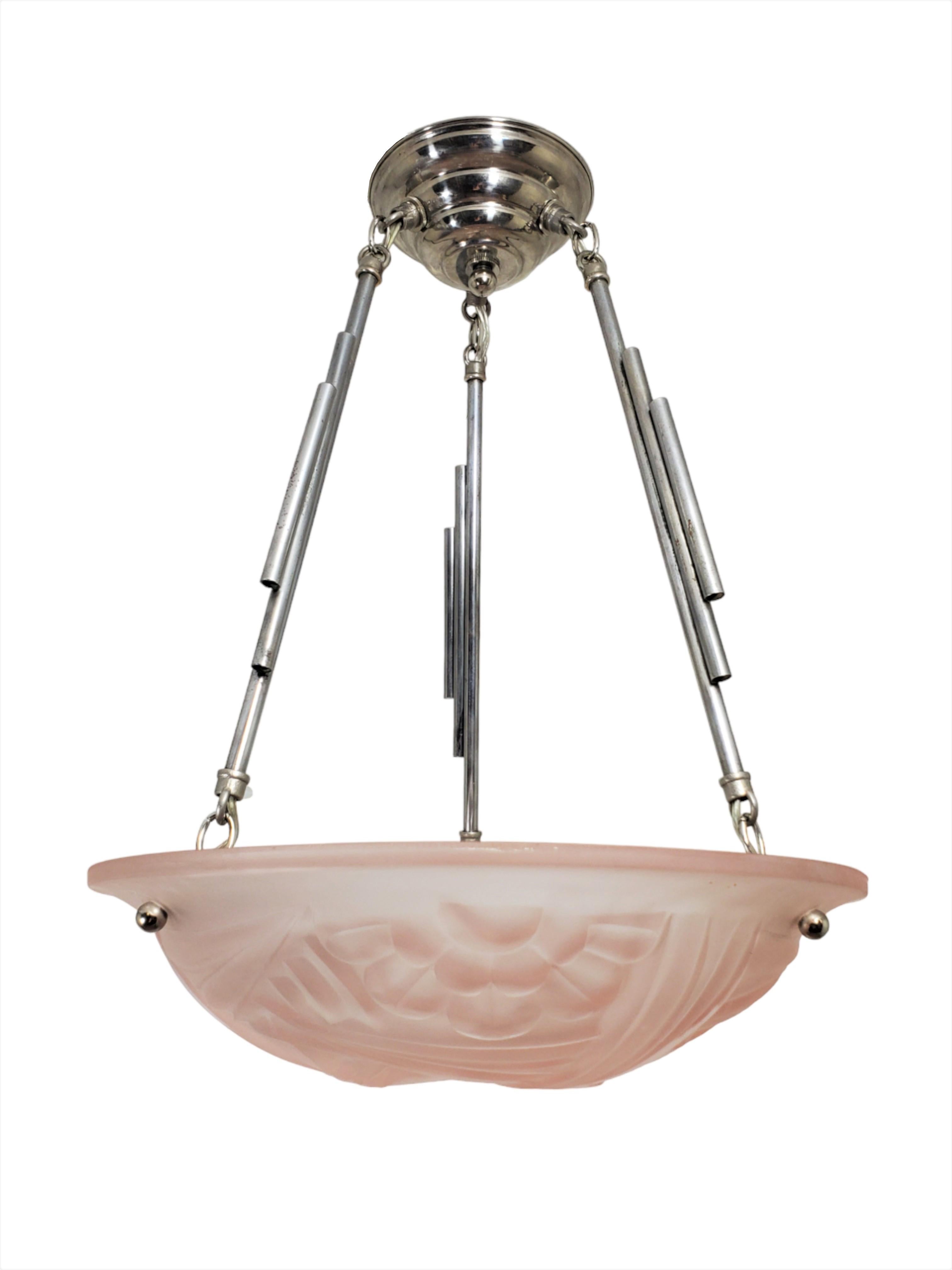 An original French Art Deco chandelier in light pink / blush frosted art glass signed Degue. The coupe showcases elegant stylized floral motifs that have been gracefully partitioned by angular, blade-like motifs. This round pendant /fixture is