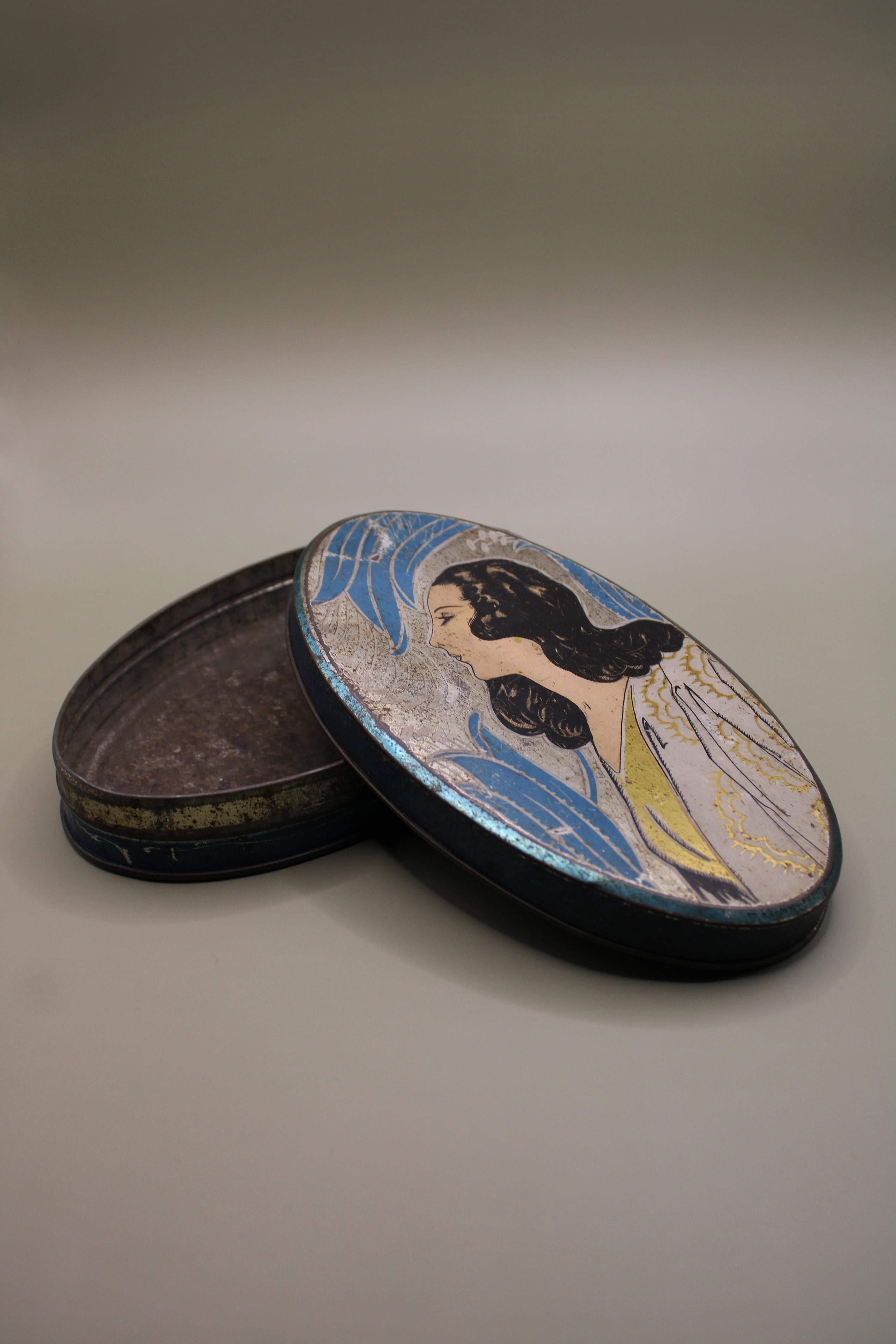 This striking and rare antique French Art Deco tin from the 1930s is a true collectible gem. A beautifully designed oval chocolate tin, it features exceptional graphics and elegant Art Deco styling, making it a standout piece for any enthusiast of