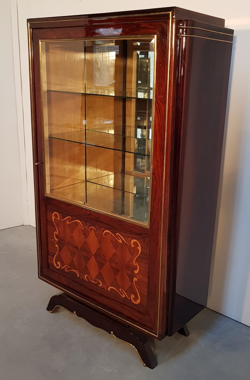 Cute art deco vitrine with lacquered palisander veneer, maple inlays and brass ornaments. Unique shape leg, inside mirror and glass-shelves, rare original key with fine metalwork. Made in France, 1930s.