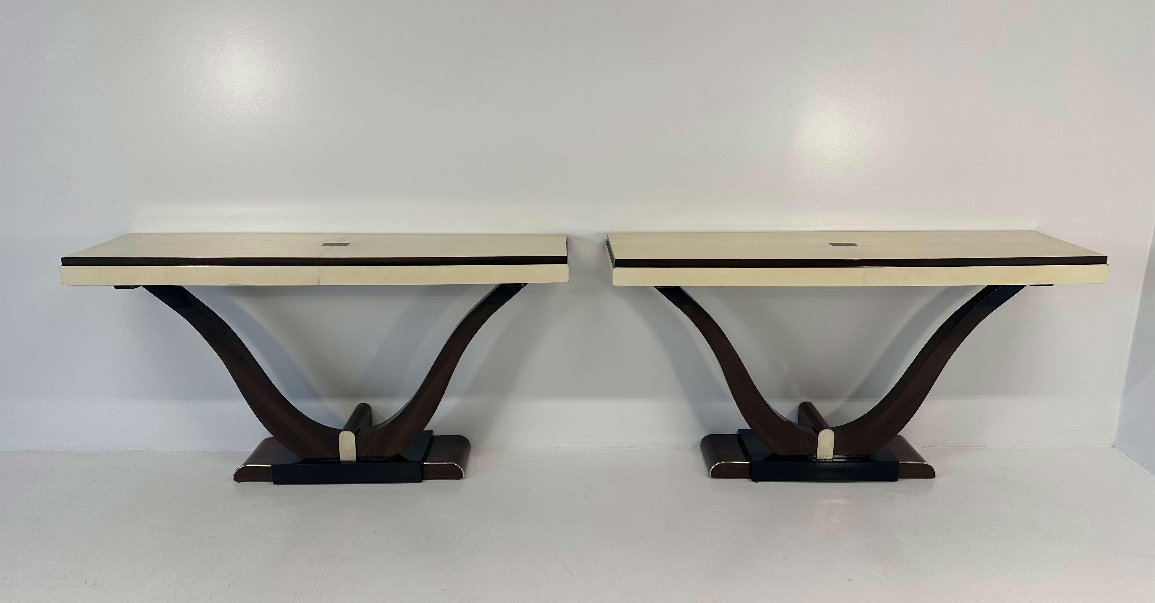 This pair of twin consoles was produced in France in the 1930s
The top, its profile and a small decorative detail on the base are in parchment. The sinuous legs, part of the base and the rectangle on the top are in exotic wood. The other parts are