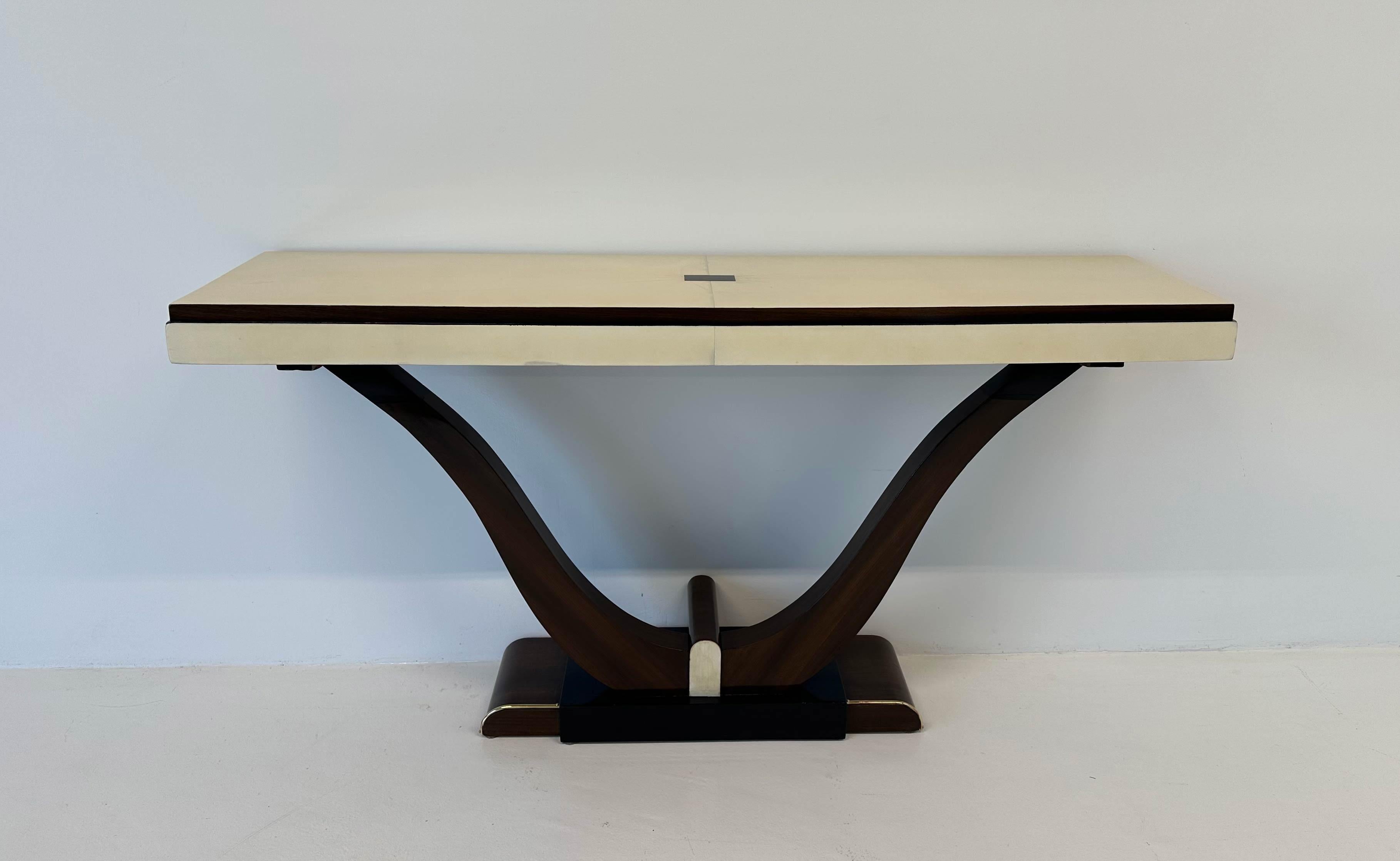 This console was produced in France in the 1930s
The top, its profile and a small decorative detail on the base are in parchment. The sinuous legs, part of the base and the rectangle on the top are in exotic wood. The other parts are black