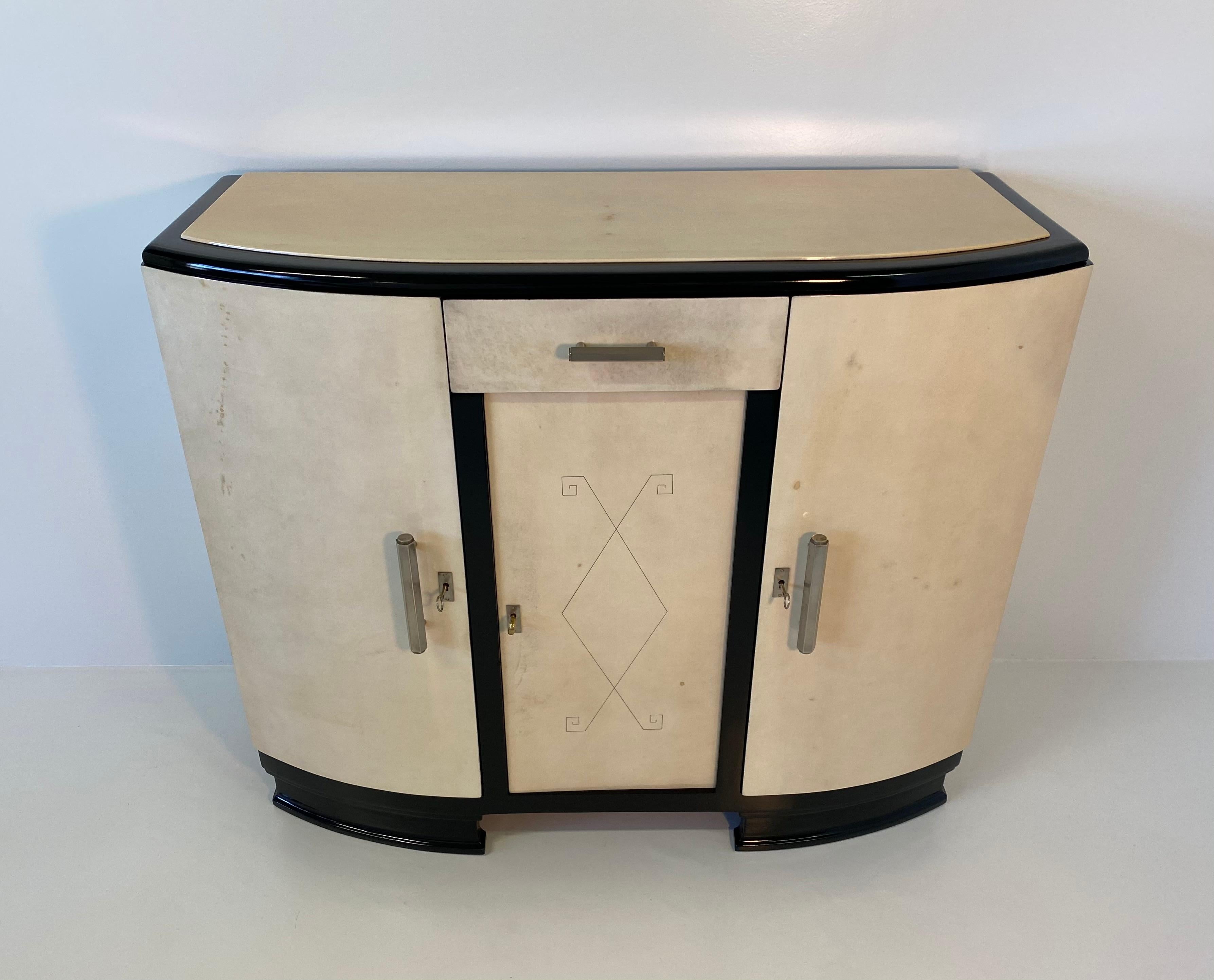 This fine and elegant Art Deco sideboard was made in France in the 1930s.
It is completely covered in parchment and It has the base and profiles in black lacquered wood.
The central decoration is engraved on the parchment and gives an unique touch