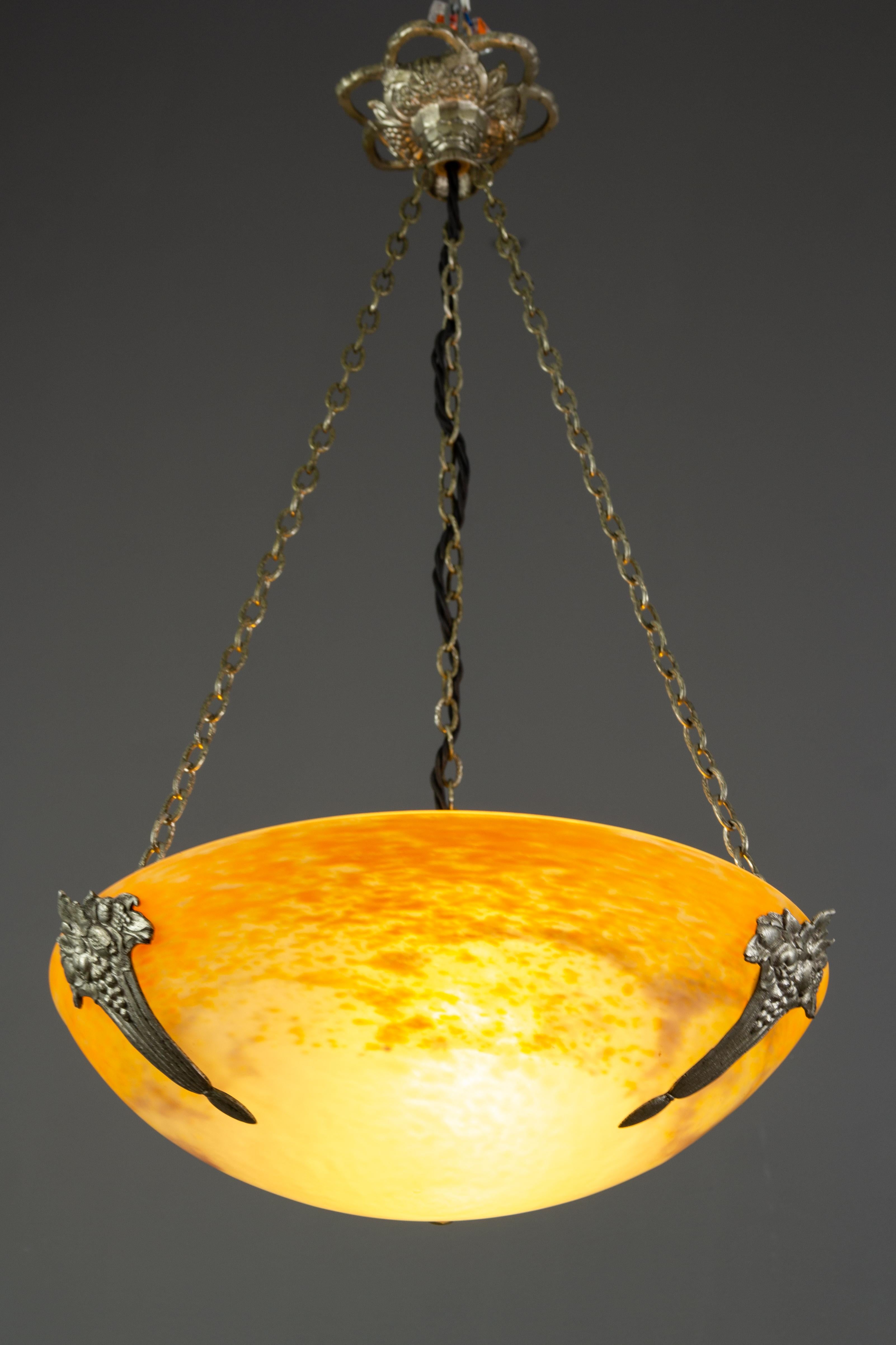 This adorable French Art Deco period pendant chandelier features a mottled “Pâte de Verre” art glass bowl in yellow, lilac, and white color, signed ”Noverdy France” by Jean Noverdy, hung at an ornate brass and silver color bronze fixture with one