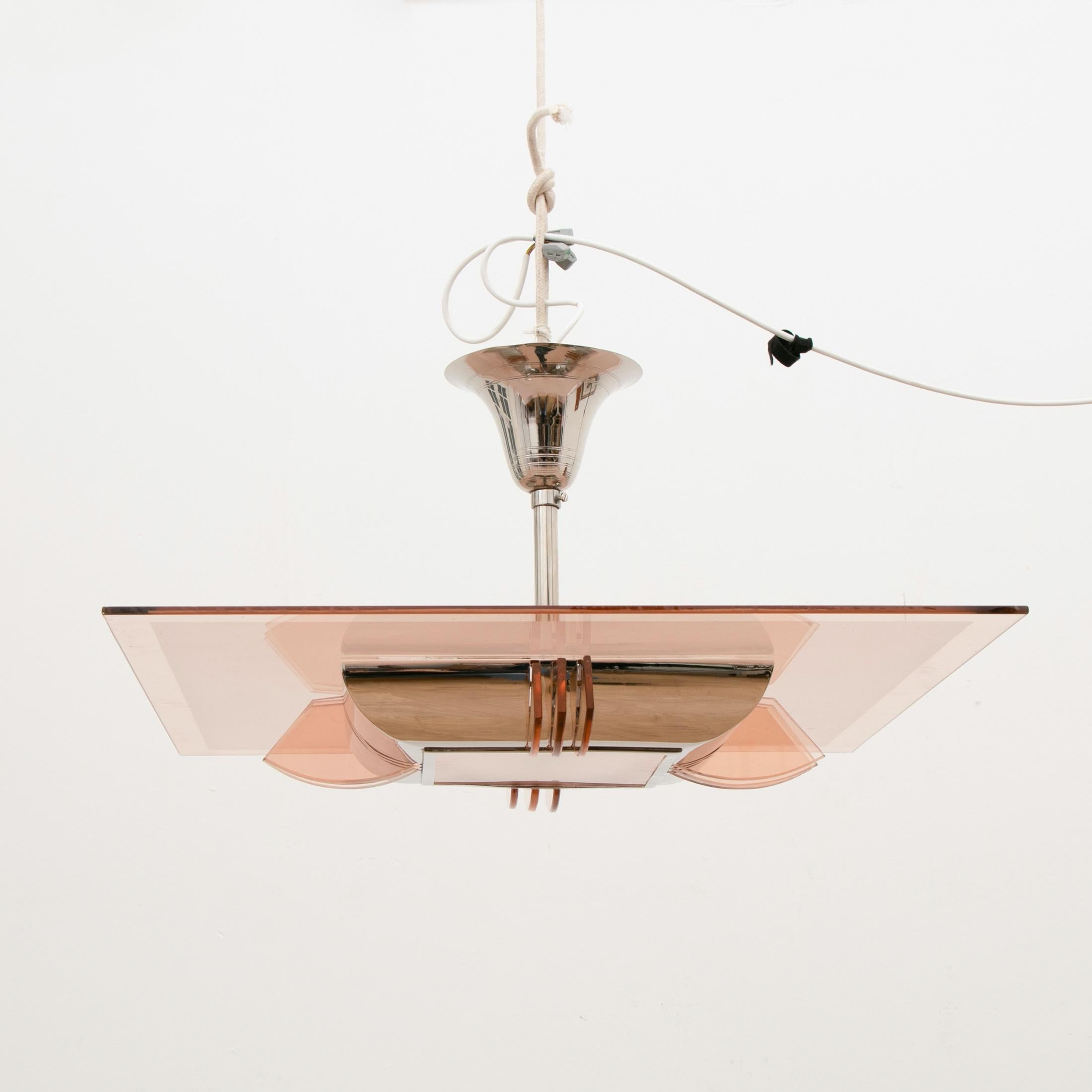 A smart modernist Art Deco chandelier by Atelier Petitot.
Square frosted peach glass with three-light transformer glass slides at the centre of each horizontal.
The square peach glass rests on a curved chrome frame, suspended on a single rod with