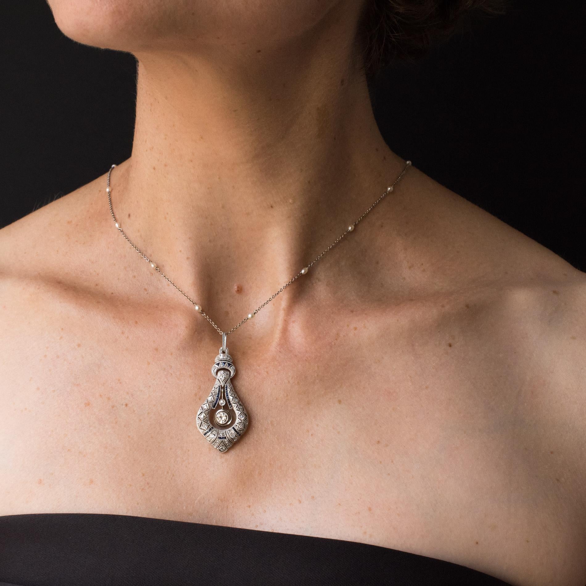 Pendant and chain in platinum, dog's head hallmark.
In the form of an articulated teardrop, this rare Art Deco pendant is decorated with diamonds and calibrated sapphires in a geometric openwork design. At the centre of the teardrop dangle 2
