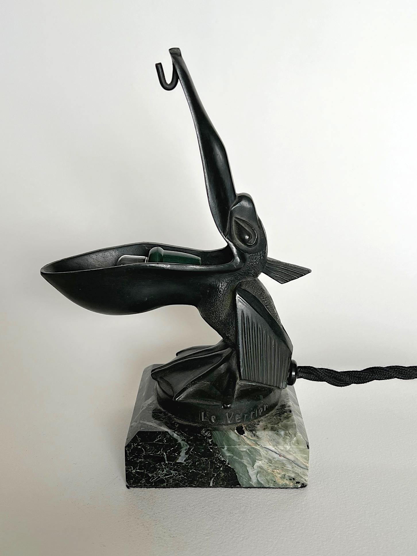 A rare combination of night light & pocket watch holder modelled as a pelican with an open beak. Cast in 'fonte d'art' - a unique alloy developed by the foundry of Max Le Verrier as an alternative to bronze - and decorated in a deep green patina.