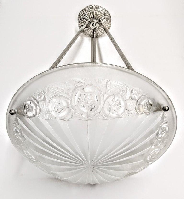 A French Art Deco pendant chandelier by the French artist “Degue“. Clear frosted molded glass shade with intricate flowers and geometric polished motif details are held by three ribbed rods with a matching canopy. The fixture has been re-plated in