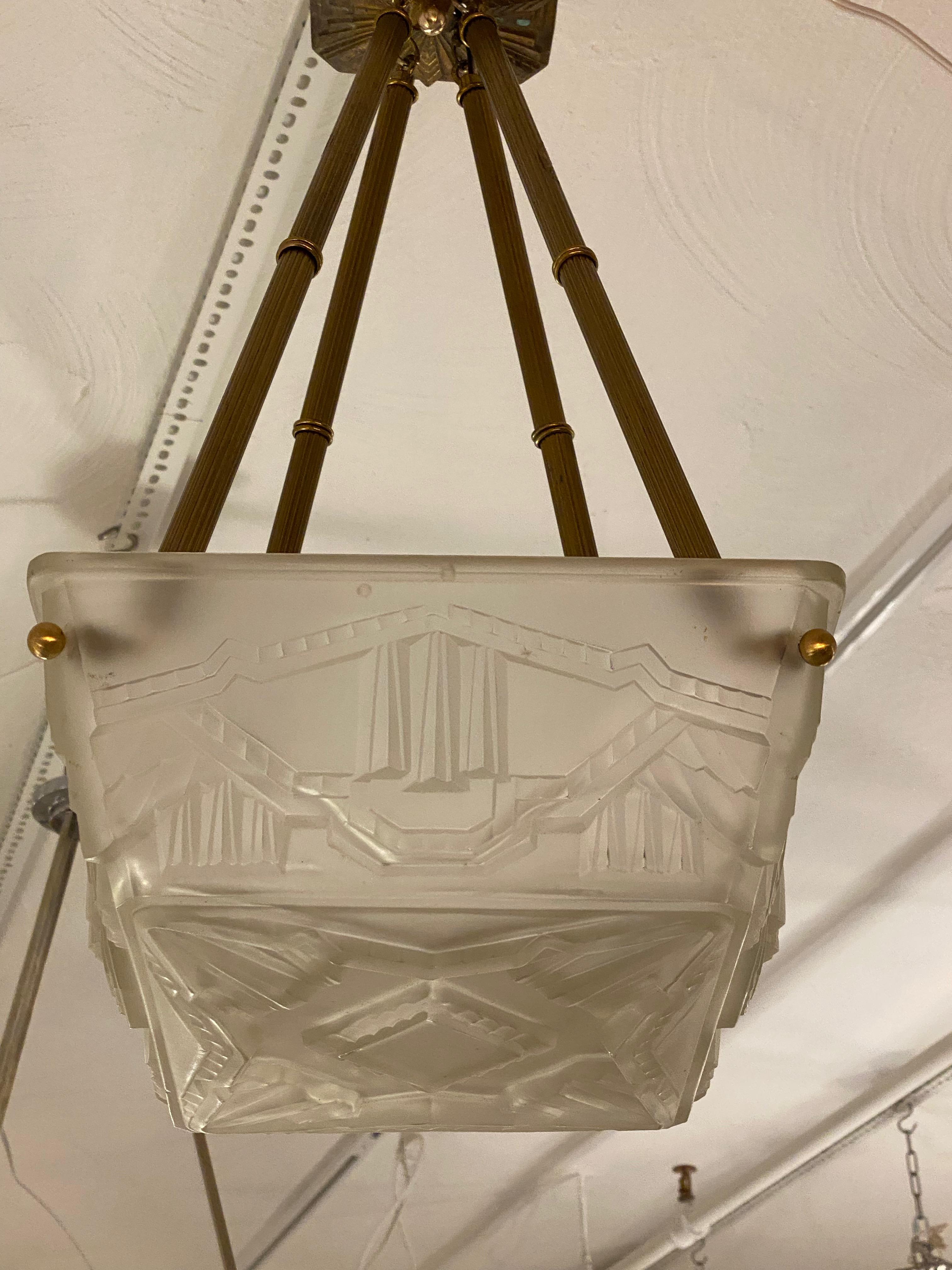 A stunning French Art Deco chandelier by the French Artist Sabino. Having a clear frosted glass square geometric  panel. Held by four brass ribbed rods. 
Intricate geometric details throughout. Plating in different finishes upon request. Has been