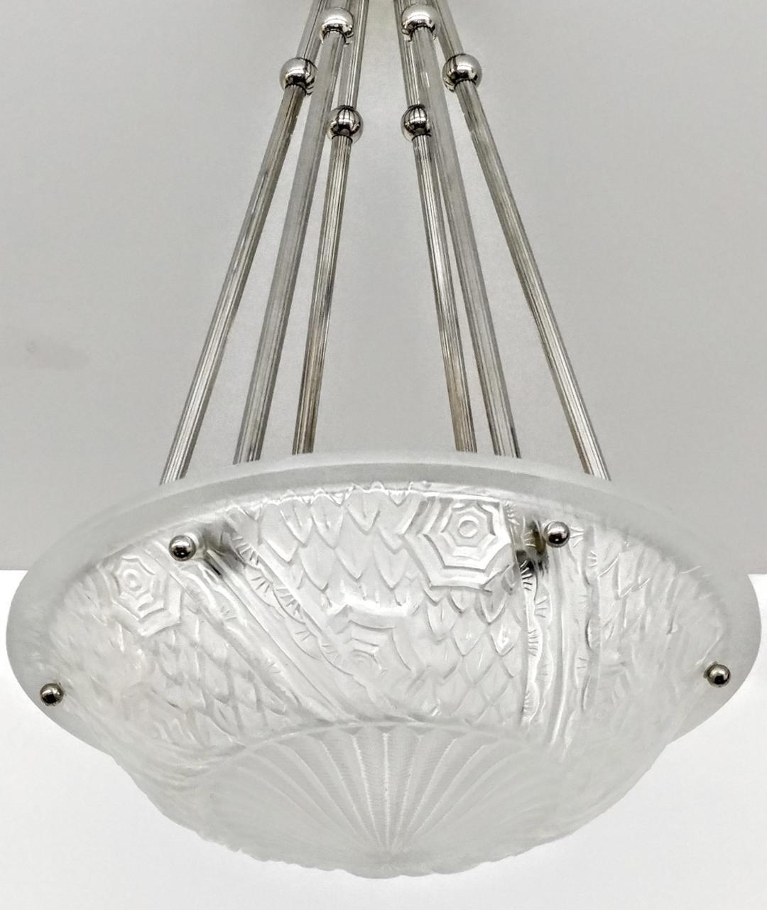 A French Art Deco pendant chandelier by the French artist “Schneider“. Clear frosted molded glass shades with intricate flowers and geometric polished motif details held by six ribbed rods with a dash of decorative balls extending from a matching