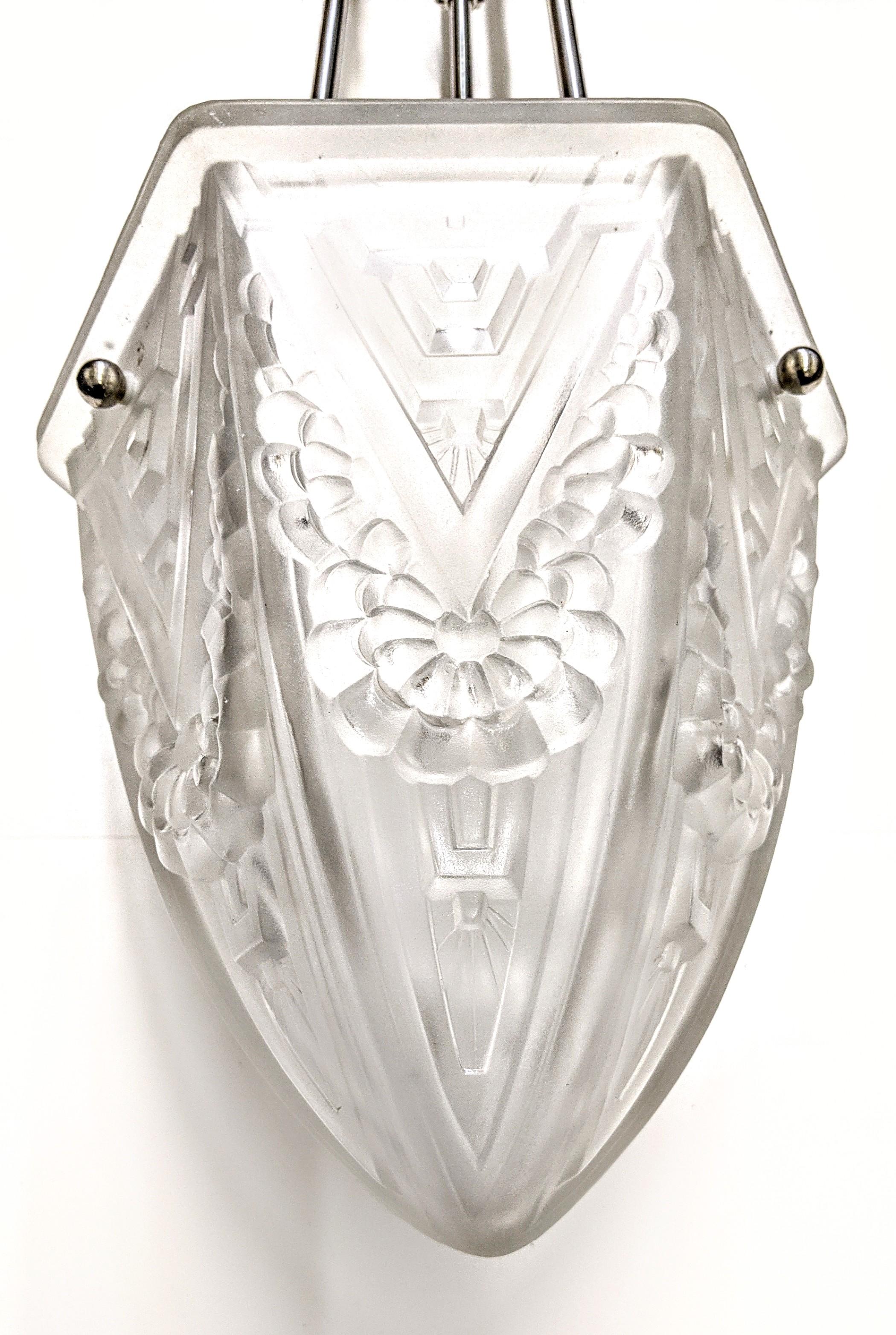 
A French Art Deco pendant chandelier with clear frosted glass shades with intricate flowers and geometric polished motif details. Held by three ribbed rods with a dash of decorative balls extending from a matching canopy. The fixture has been