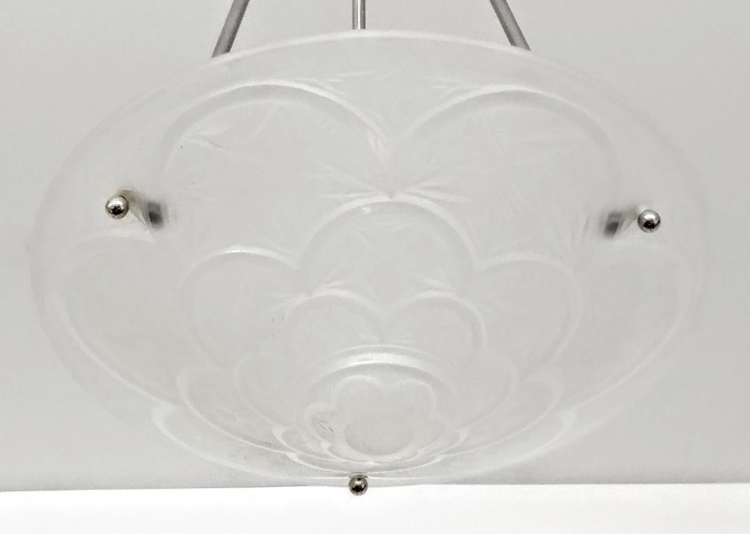 A French Art Deco pendant chandelier by the French artist “Hanots“. The clear frosted molded glass shades with intricate geometric polished motif details. The shade is marked HANOTS FRANCE. Held by three smooth rods with decoration held by a