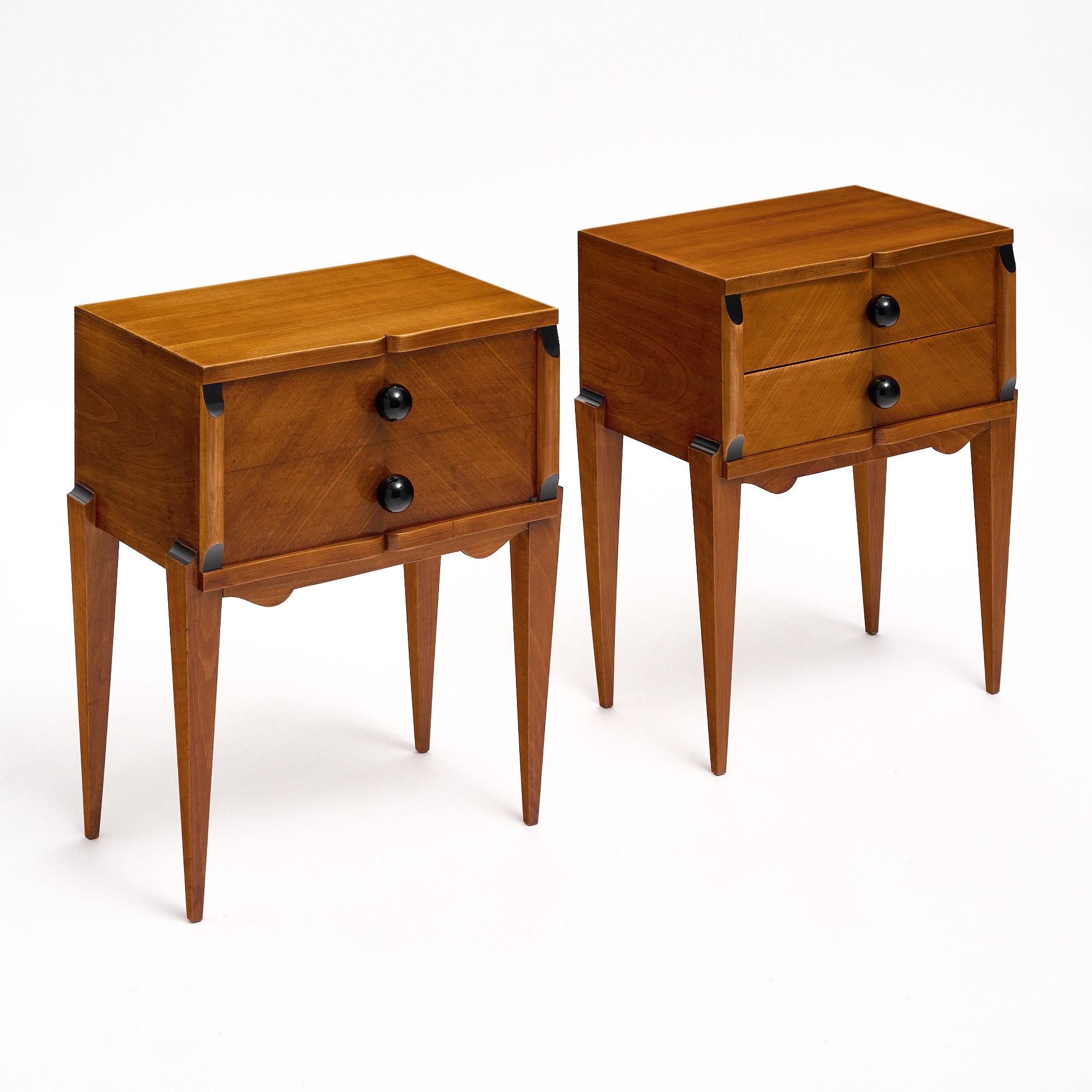 Side tables from the Art Deco period in France. This striking pair is made of rosewood and features the stylized curves and tapered legs and details iconic to the Art Deco period. Each table has two dovetailed drawers that feature black Murano glass