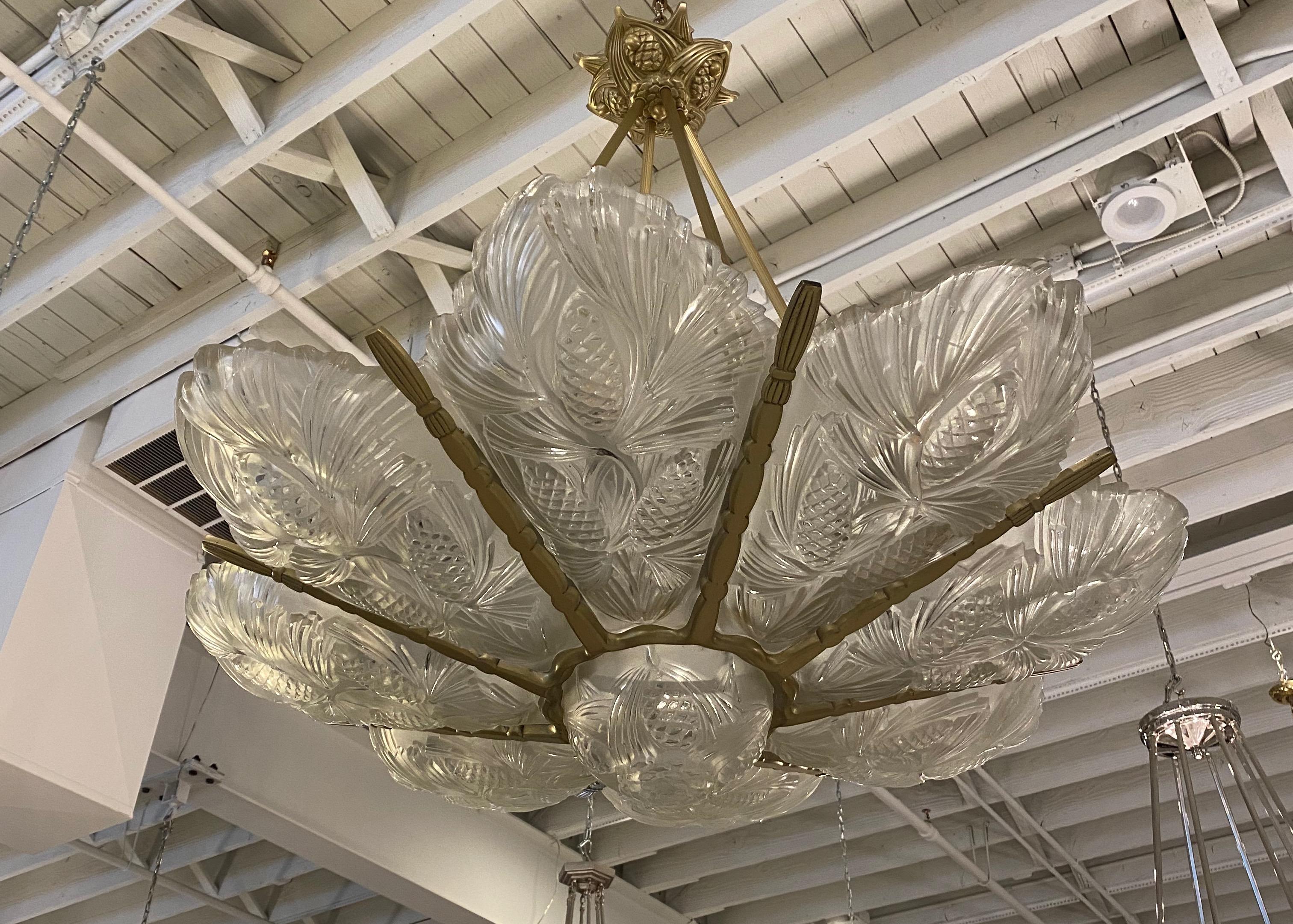 French Art Deco chandelier signed by famous artist Sabino. Having Eight outer panels and center bowl with pine cone motifs. The glass rest in a brass design frame. The pine cone motif continues on the ceiling plate. The chandelier has been fully