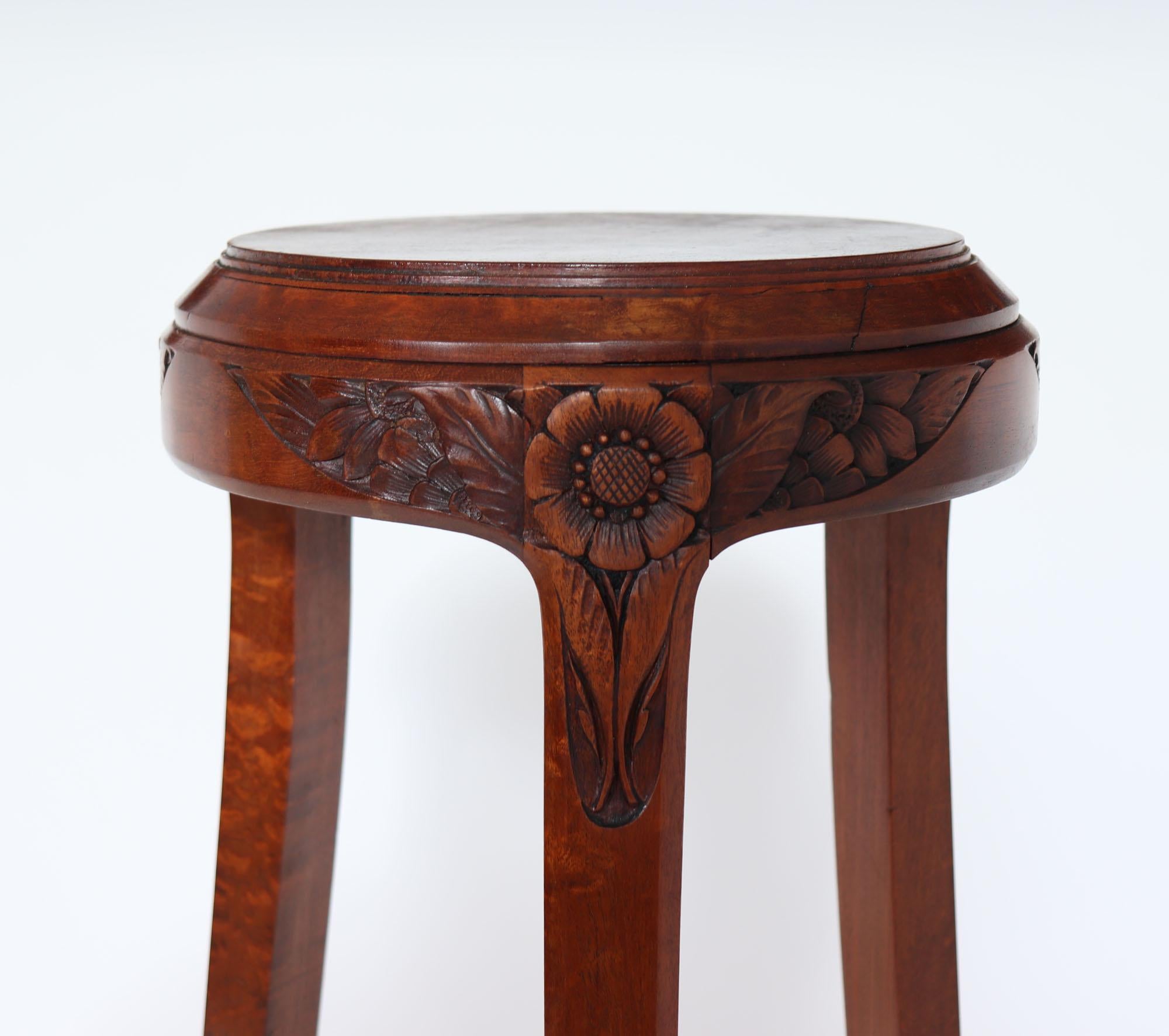 A stunning tall plant stand in solid pomelle sapele, by Paul Follot c1925, it has a circular top with three legs supporting a triangular shelf, at the top of each leg there are crisply carved flowers in bird form, each one unique. The table is in