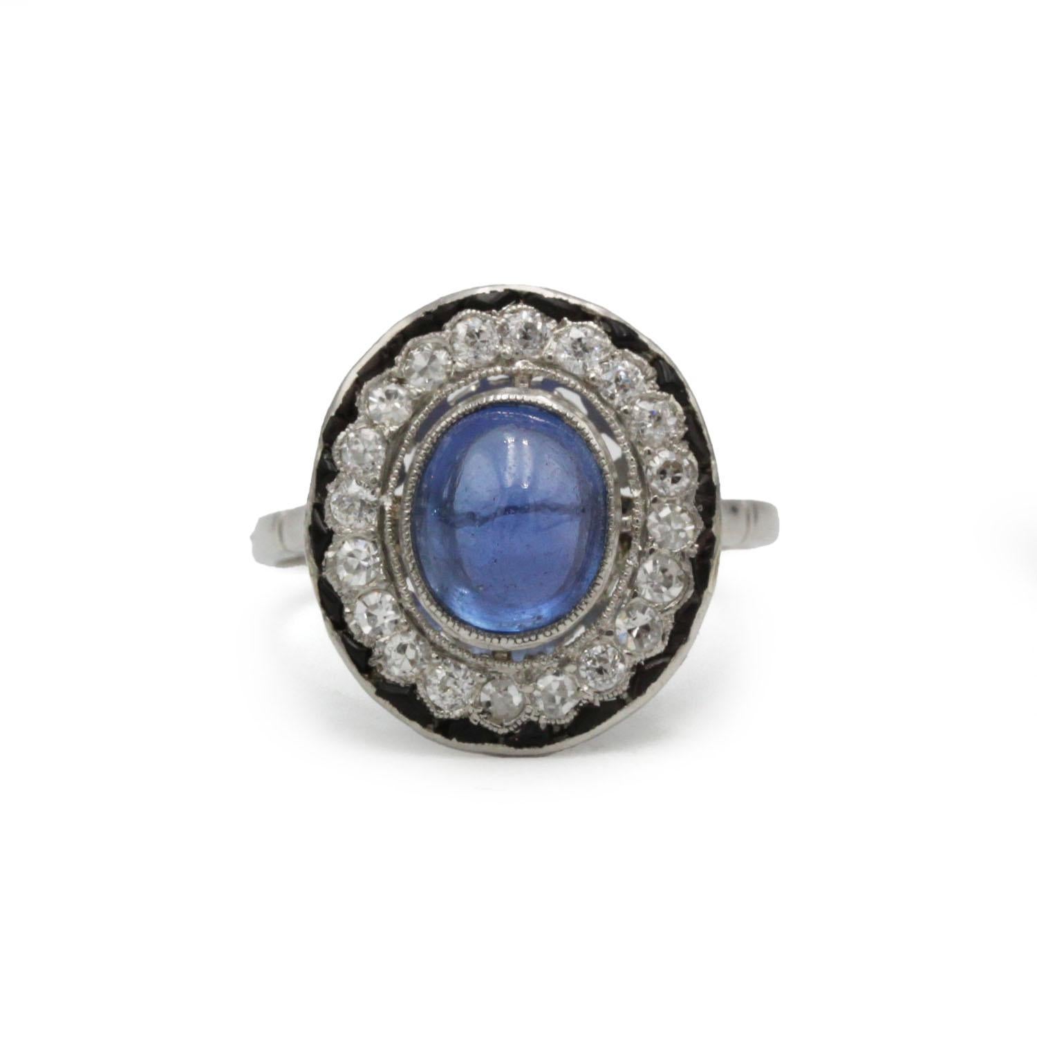 Une bague Art déco française élégante et intemporelle, centrée sur un magnifique saphir cabochon bleu naturel, encadré par un halo de diamants de taille ancienne et souligné par une bordure d'onyx noir saisissante. La galerie ajourée révèle finesse