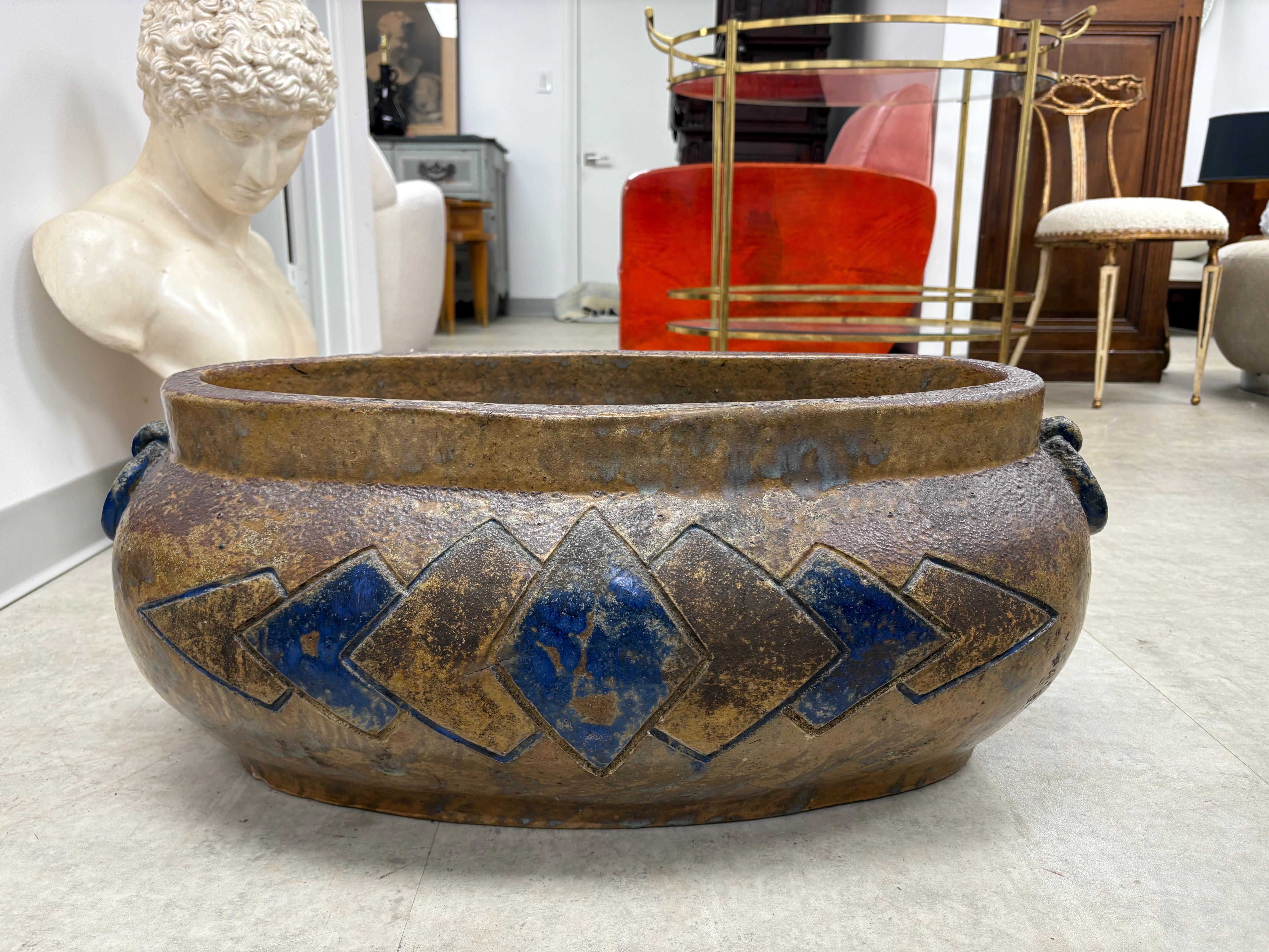 French Art Deco Pottrery Jardiniere.
Offered is a spectacular period French Art Deco pottery jardiniere. This stunning large scale matte glazed oval pottery jardiniere has a stylized geometric design on both sides with circular handles and a