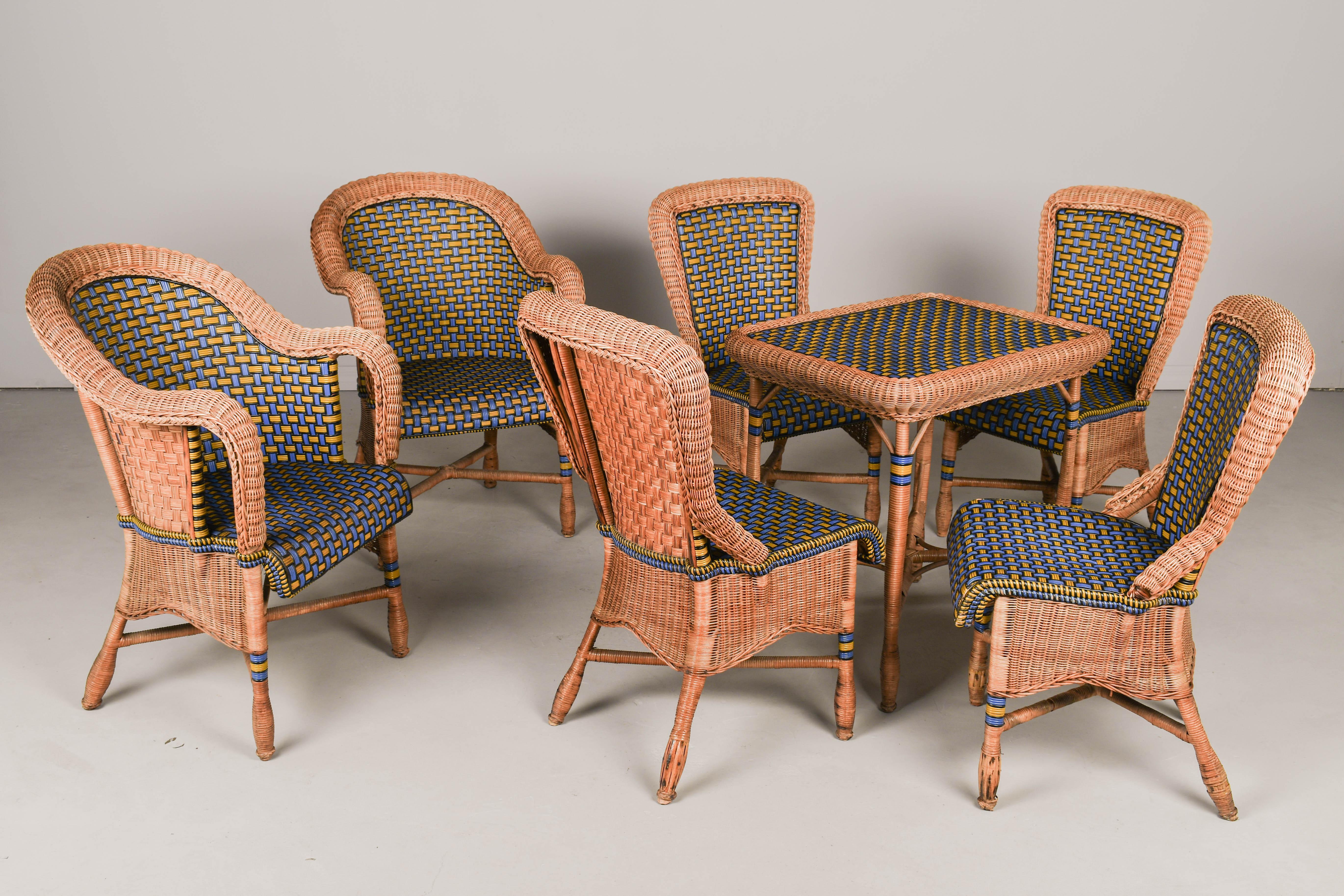 Ensemble de patio Art déco français comprenant une table, quatre chaises d'appoint et deux fauteuils, chacun avec un cadre en osier joliment tressé à la main et une assise et un dossier noir joliment ornés de motifs bleus, jaunes et noirs. Robuste