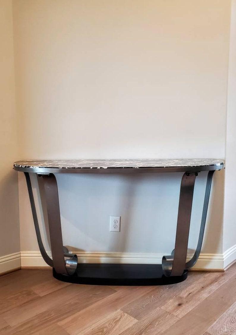 A large and impressive, circa 1930s, Art Deco scrolled steel marble-top demilune console table, attributed to iconic French designer Raymond Subes (1891-1970). Having a dramatic black white veined marble top supported by a curlicue apron with four
