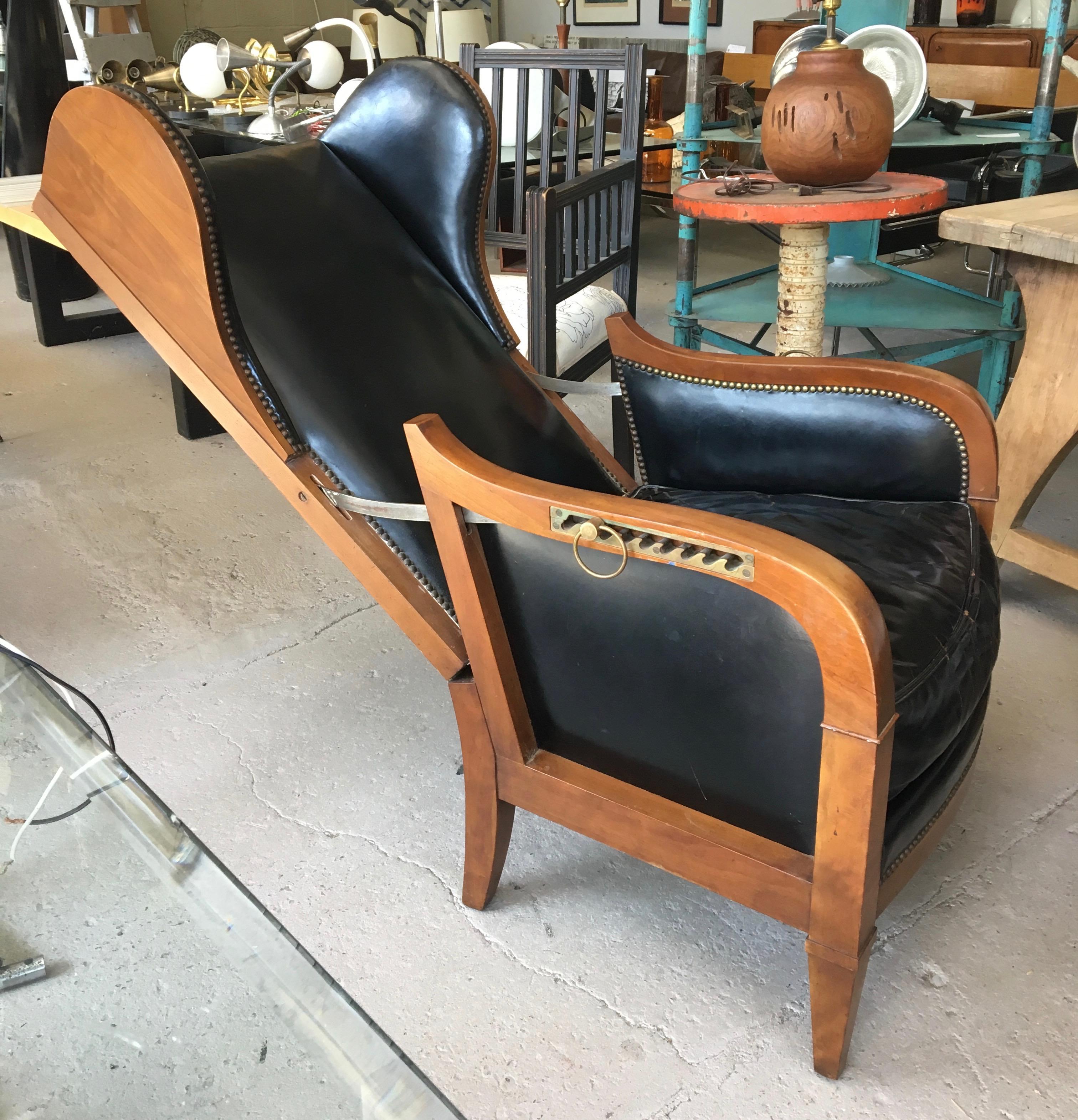 Clever and handsome 1950s French Art Deco style adjustable back wing chair in walnut wood with solid brass adjustable back mechanism. Original black leatherette is distressed but chic, brass nail heads; the chair back reclines easily.