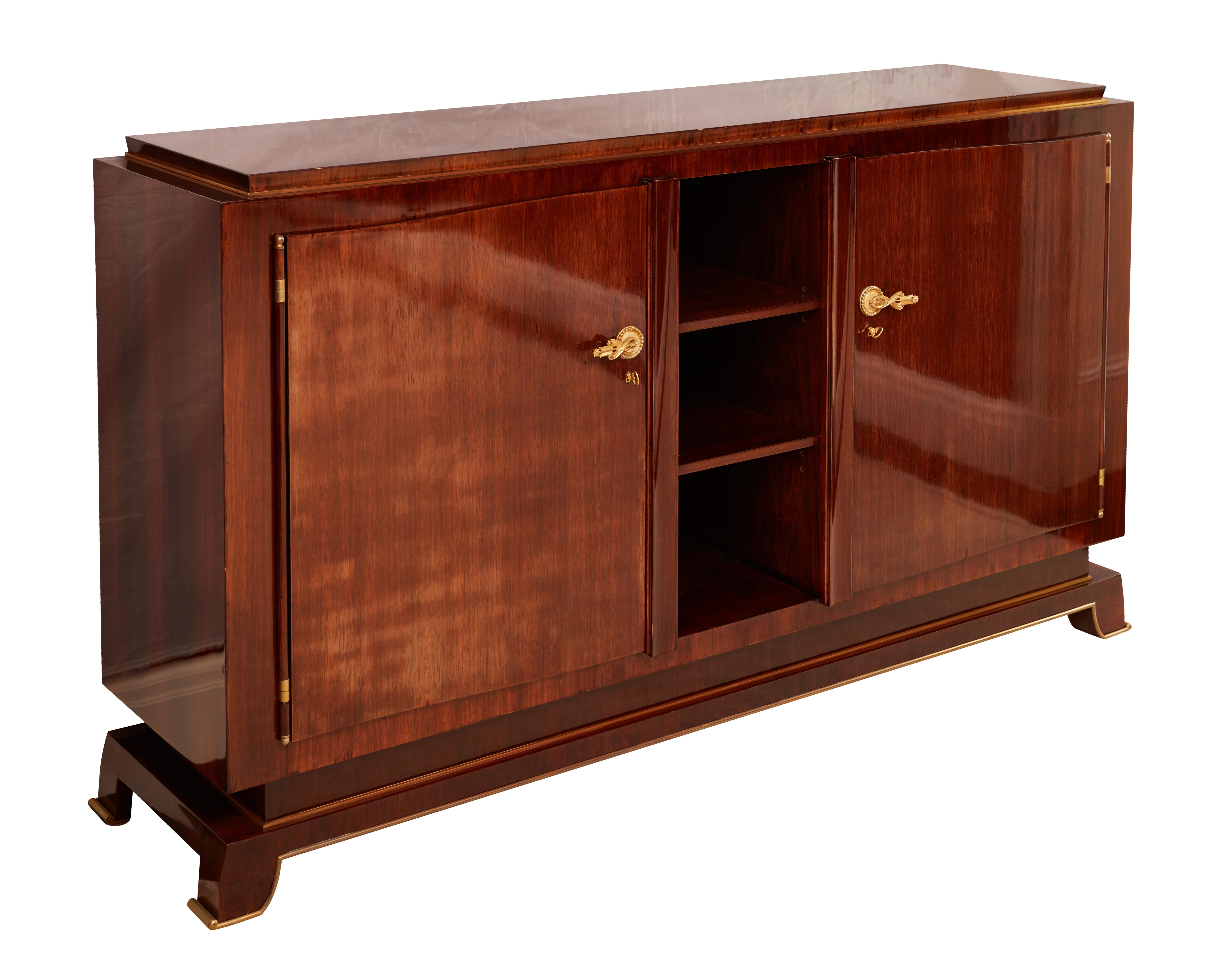 Un raffinato mobile a due ante in palissandro di Jules Leleu con ornamenti in bronzo dorato disegnati da Debarre e cesellati da Perret. Due ante che si aprono per rivelare un interno con cassetti e scaffali. Timbro e stampigliatura sul retro 23758.