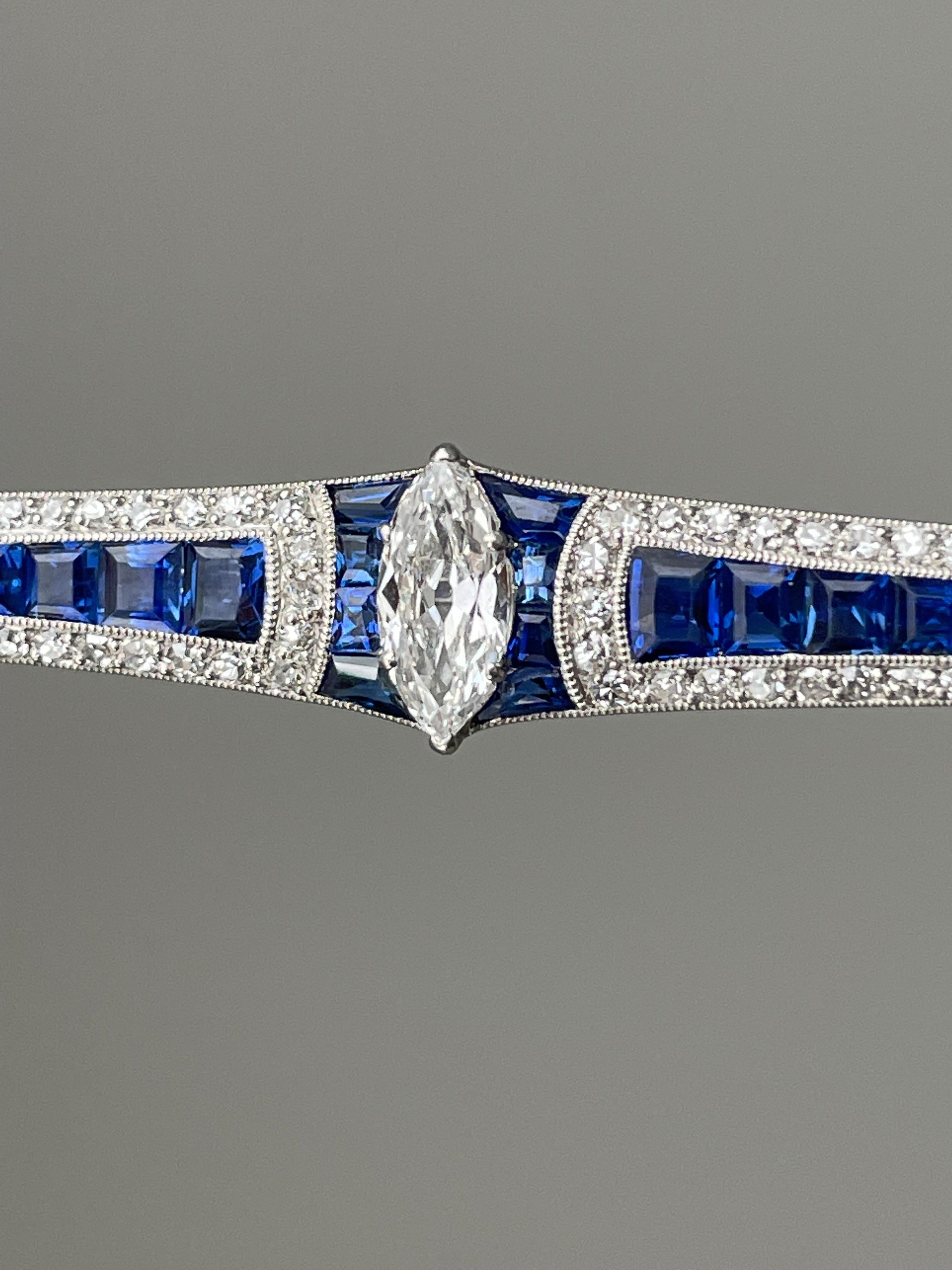 Both elegant and pristine, this French Art Deco brooch centers on a scintillating .85 carat (VS1 / G-H) marquise-cut diamond bordered by seamlessly-set natural blue sapphires that flow into a gently graduated line of brilliant blue sapphires, framed