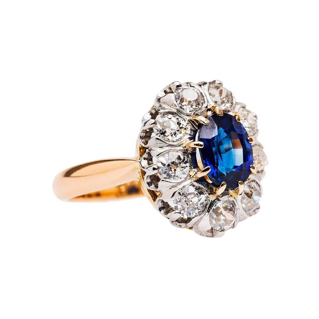 Art Deco is a style of visual arts combining architecture and design that first originated in France before the commencement of the first world war. Featuring a natural royal blue sapphire that is crowned by a halo of 9 old cut diamonds. Hand
