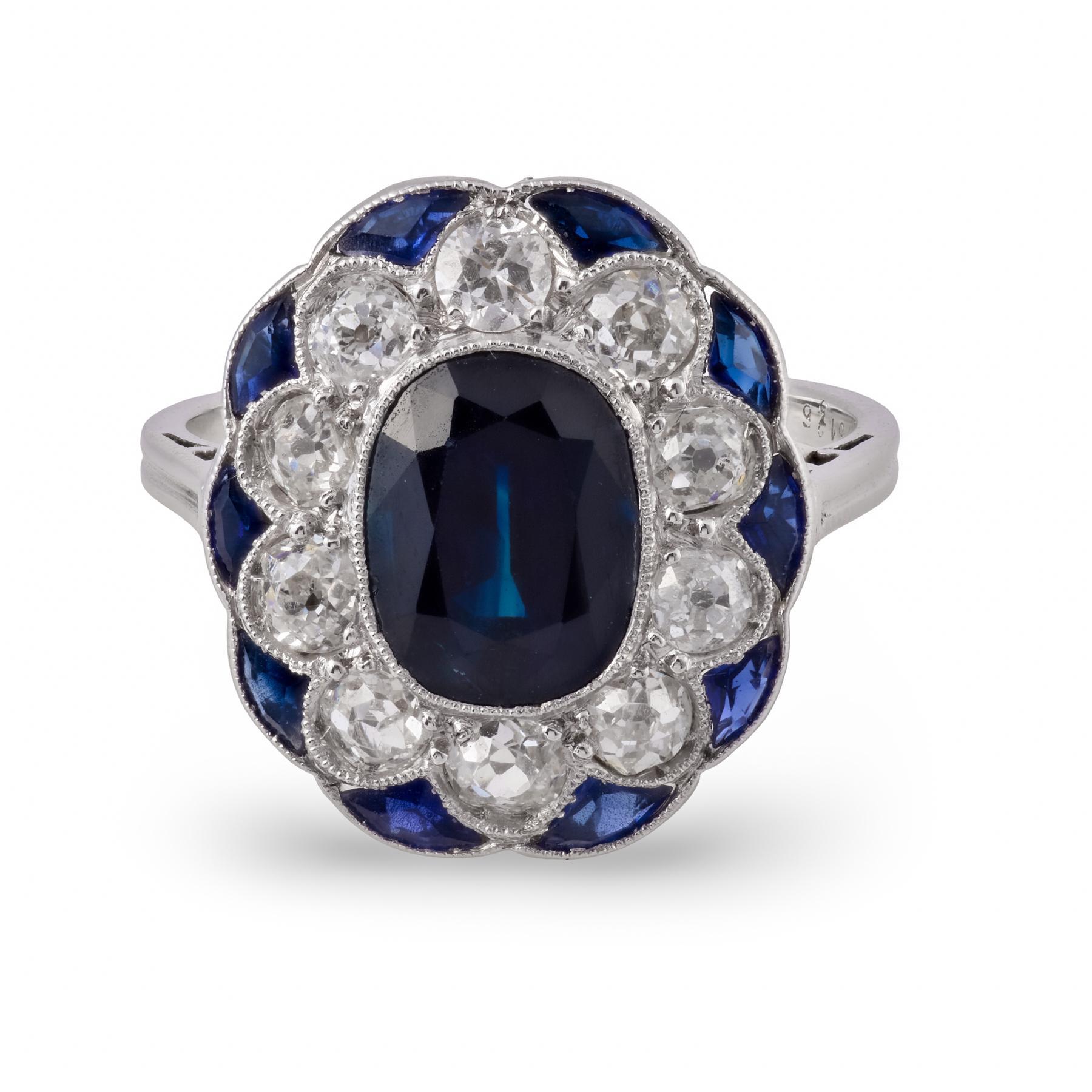 Cette bague de table Art déco française est centrée sur un saphir bleu richement saturé dont la forme ovale rayonne de couleur et d'élégance, entouré d'un arrangement précis de saphirs taillés en calibre qui créent un équilibre géométrique