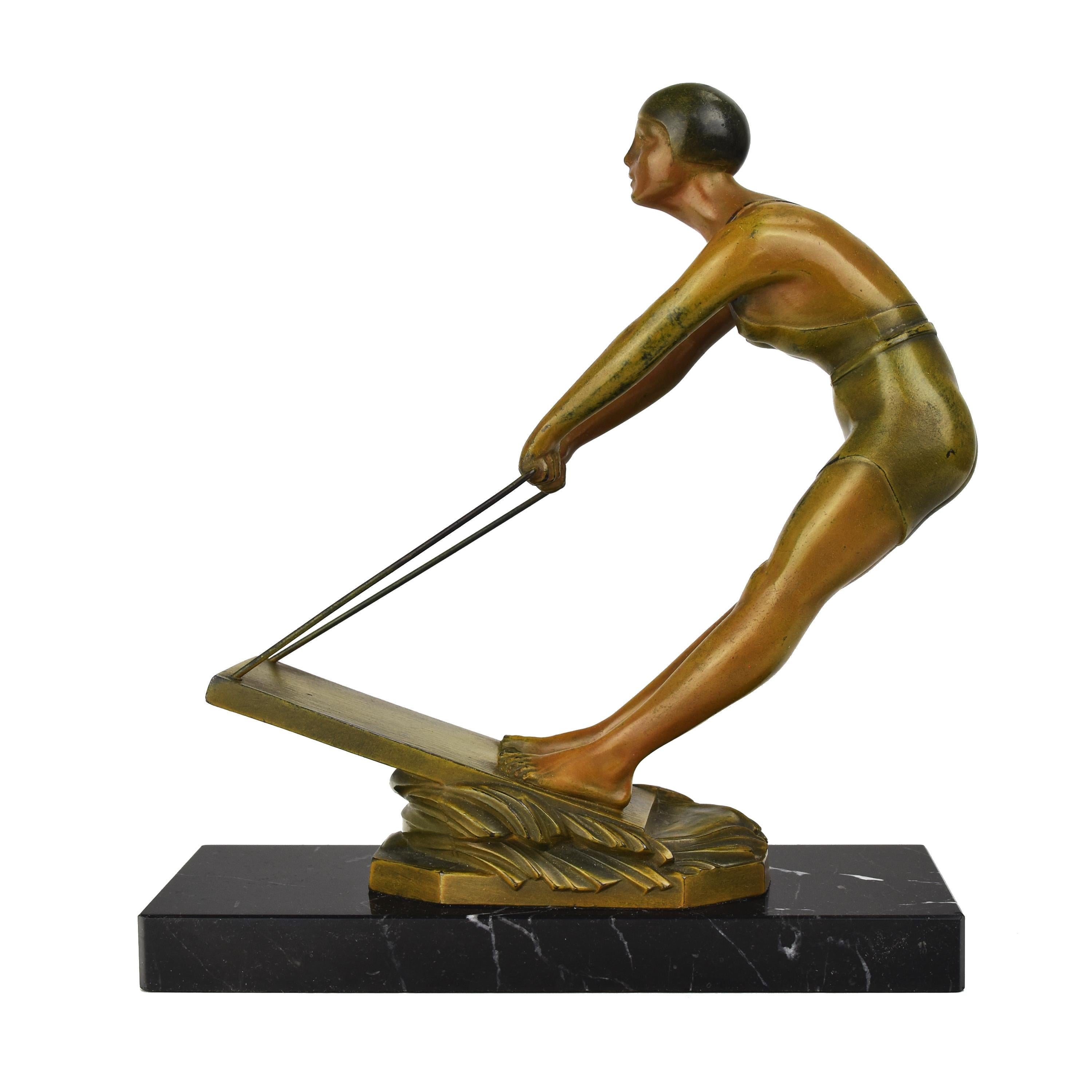 Cette sculpture représente une femme en train de faire du wakeboard dans une pose dynamique, tenant fermement la poignée attachée au wakeboard sur les vagues. La figurine est vêtue d'un maillot de bain moulant et porte un bonnet de bain. La