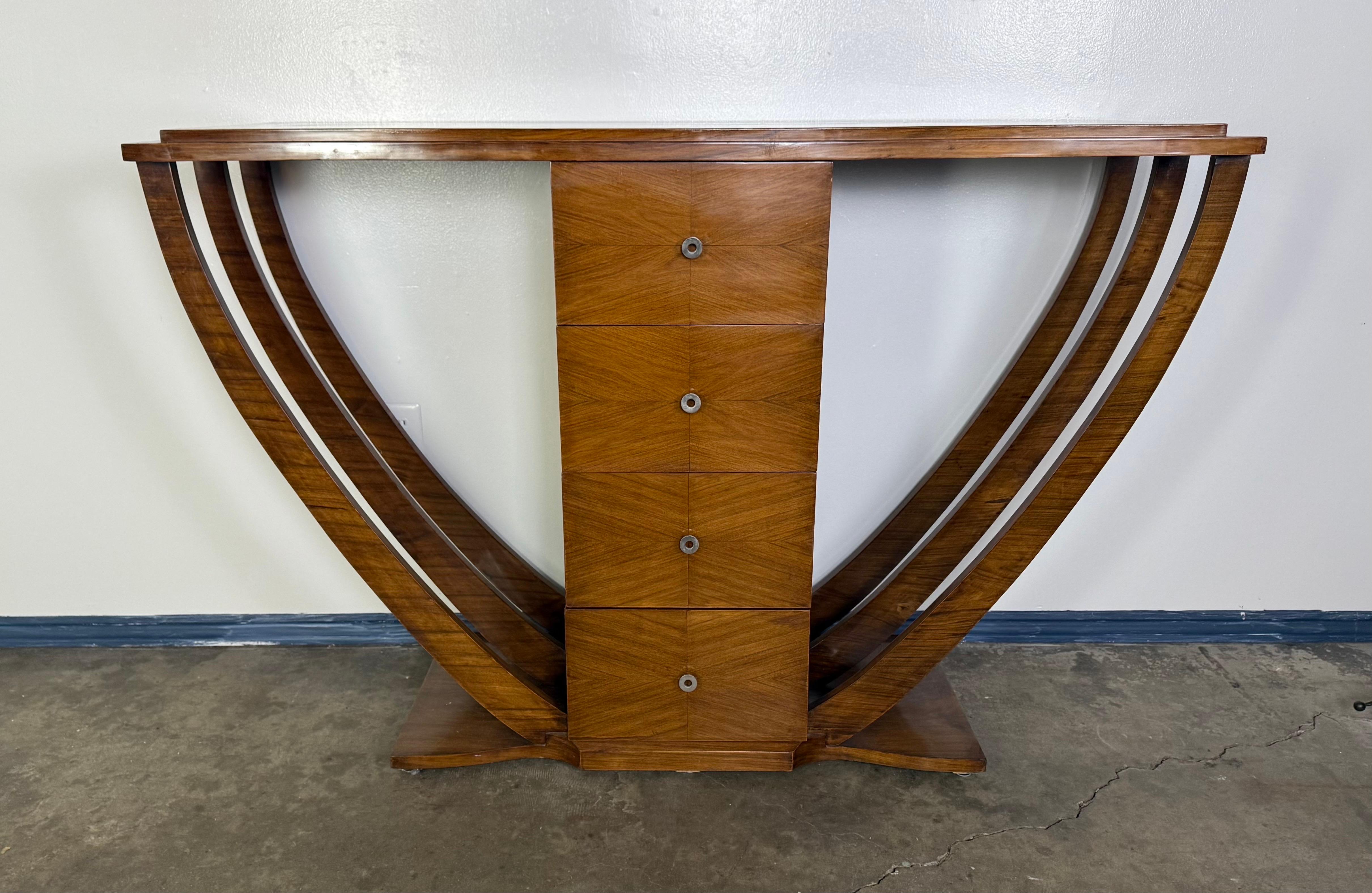 Cette étonnante console Art déco présente une silhouette audacieuse et symétrique centrée sur un empilement vertical de quatre tiroirs dotés d'élégantes poignées circulaires en métal. Le design présente des lignes architecturales audacieuses avec