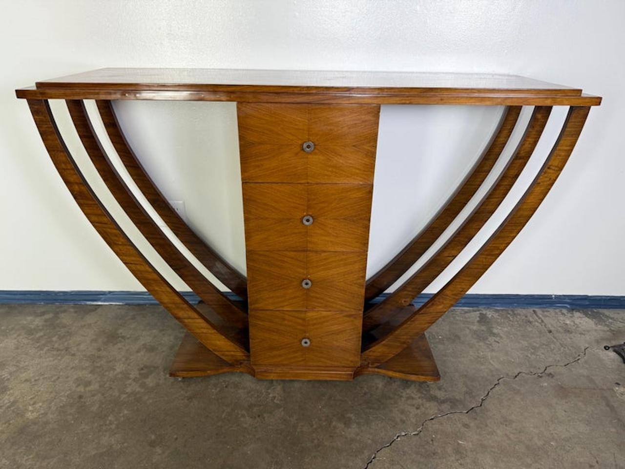 This striking Art Deco console features a bold, symmetrical silhouette centered around a vertical stack of four drawers with sleek, circular metal pulls. The design features bold, architectural lines with a dynamic curved form that is distinctly