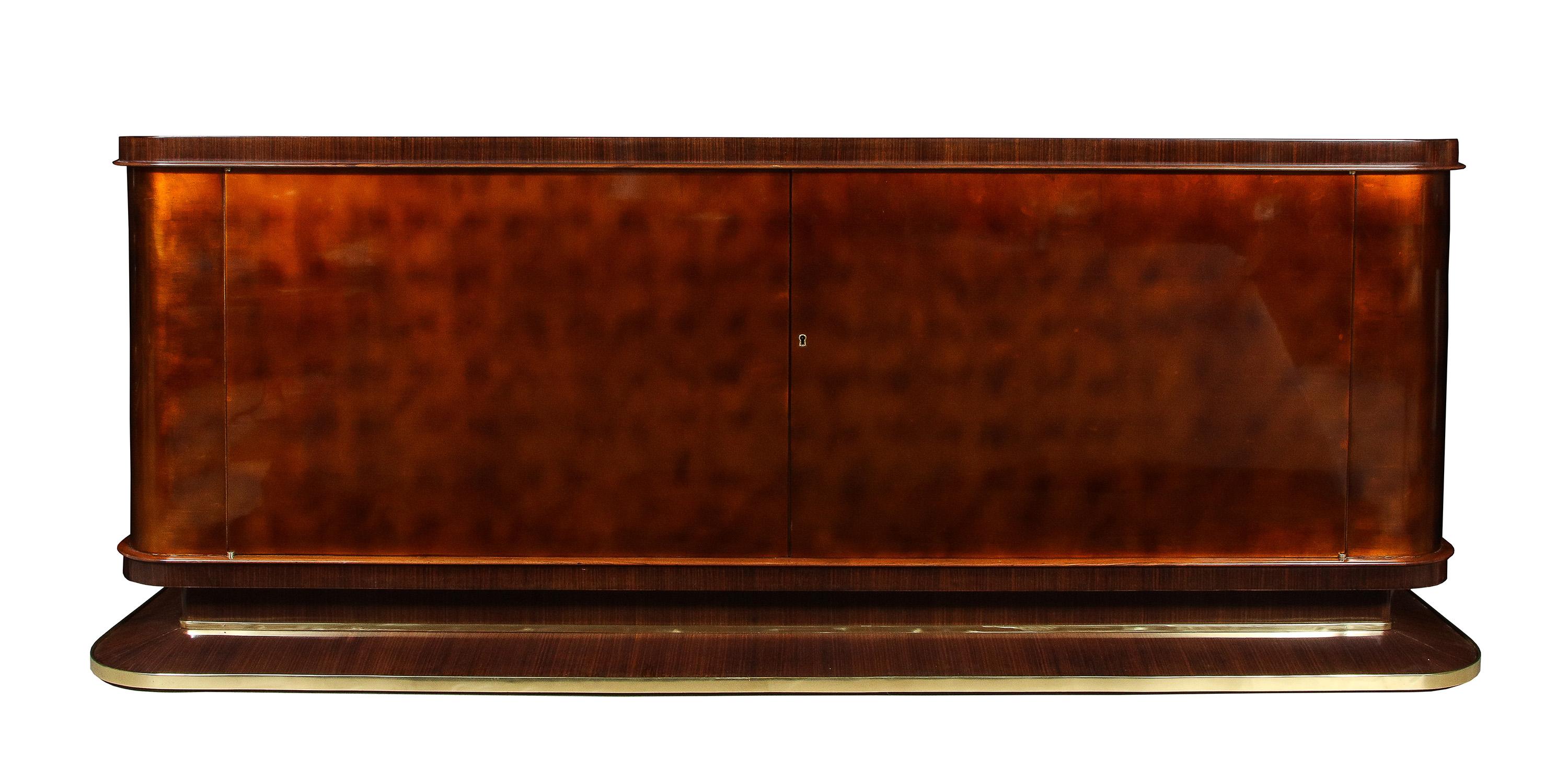 Of rounded form, having a Rosewood top and plinth edged with brass straps. The doors and body lacquered in deep caramel over gold leaf, the two doors opening to a fitted sycamore interior.
Paper label: GRAND MEUBLE PUBLIC, 17 RUE MONSIGNY PARIS