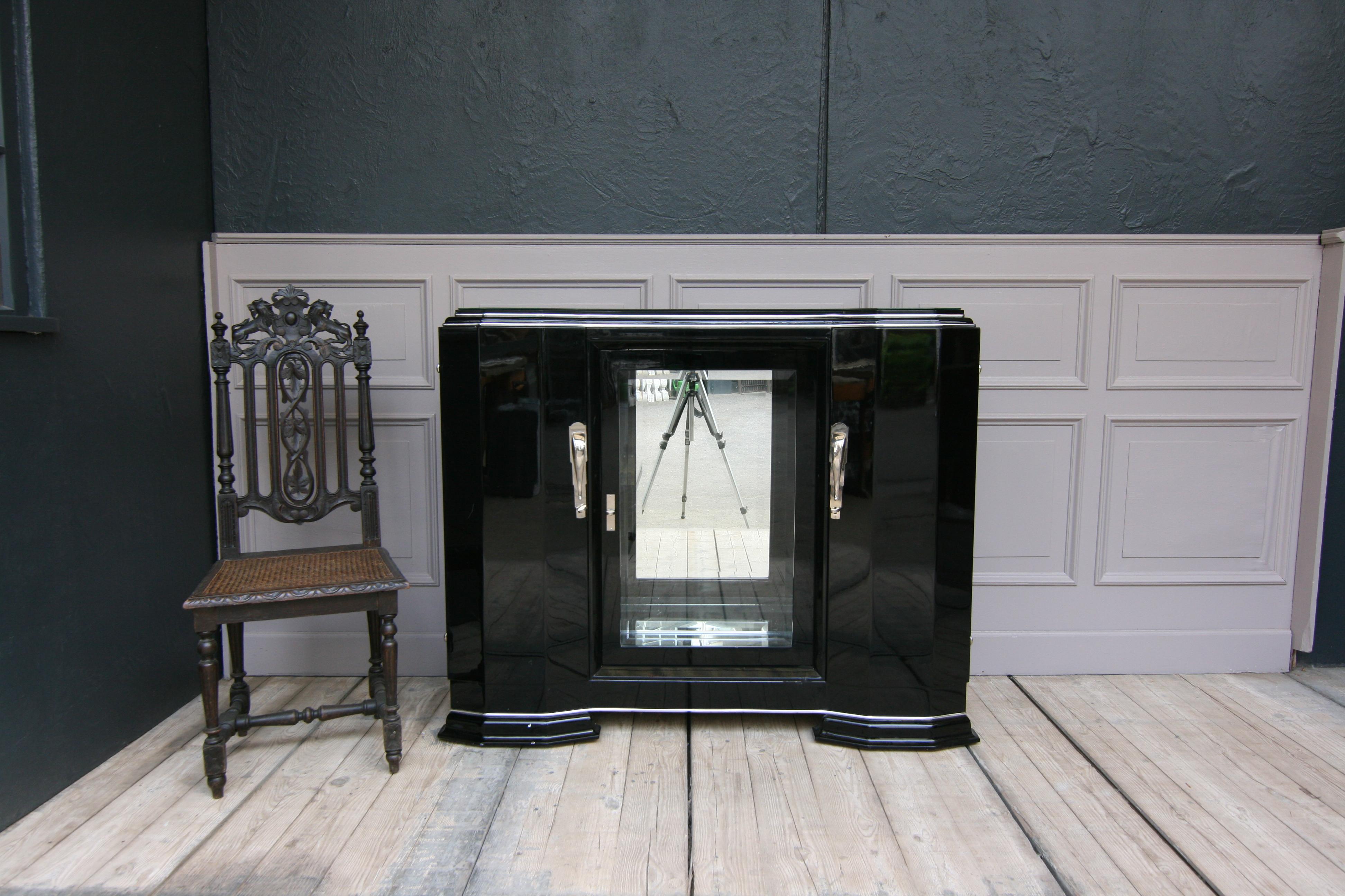 Original Art Deco sideboard from France in black high gloss, unrestored.
Left side and right side, each with a door with a shelf behind it. In the middle is a glass door with faceted cut glass. Mirrored behind, rear wall and floor. 2 glass