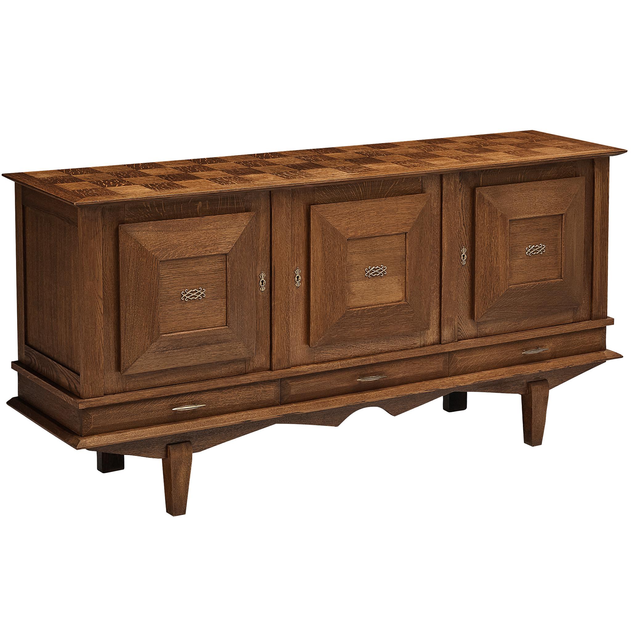 Sideboard, oak, brass, France, 1940s

Three-door sideboard with Art Deco characteristics. The geometrically inlayed top and attentively designed doors, contribute to a special design. With its three-dimensional feel, the sideboard lays full focus on