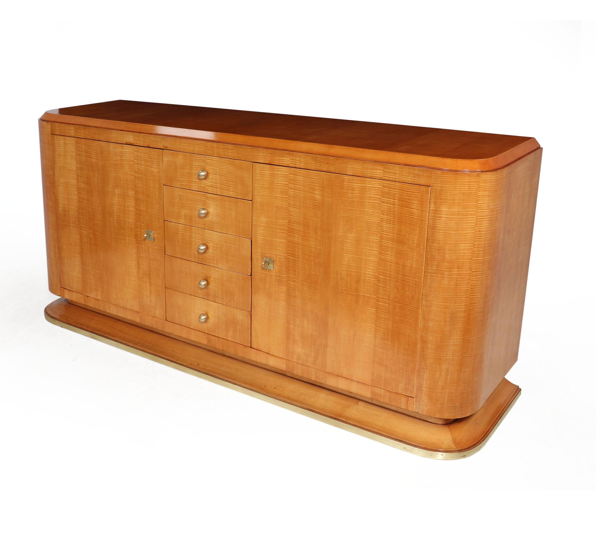 This French Art Deco sideboard in Sycamore wood is a stunning piece of furniture that offers both style and storage. This stunning piece features two lockable doors with five central drawers and ornate brass ball handles. The top surface provides