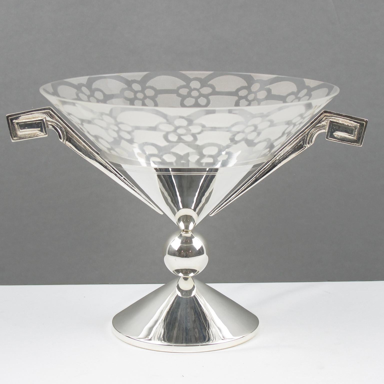 Este elegante centro de mesa o cuenco decorativo Art Decó francés tiene forma de alto pedestal en metal plateado con grabado y grandes asas geométricas. La pieza se fabricó hacia 1930. El cuenco de inserción es de vidrio soplado transparente con un