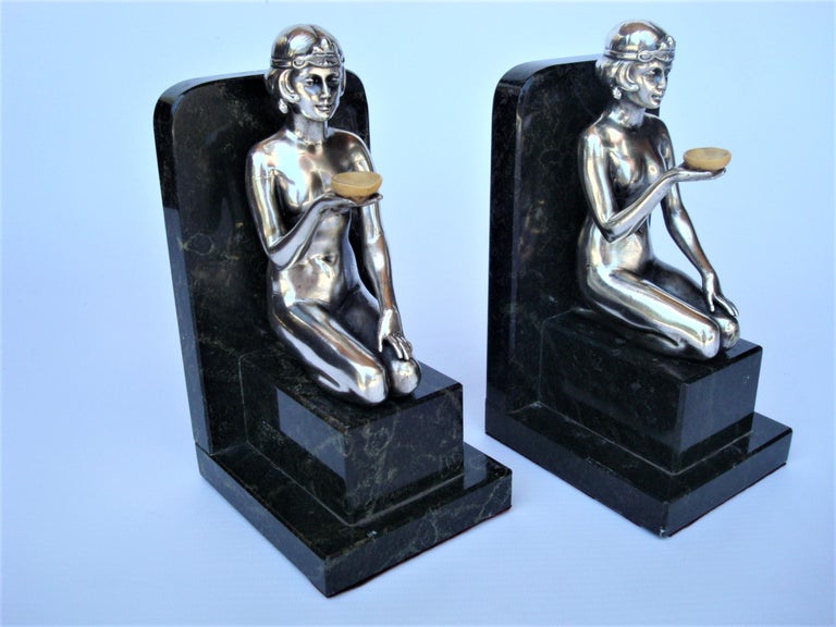 Art Deco women silvered sculpture bookends. 
It stil has the original sticker of the shop that sold it.
Art Deco figures in silver of two women as bookends on green marble bases. 
These classic deco statuettes are beautifully rendered,. Take a