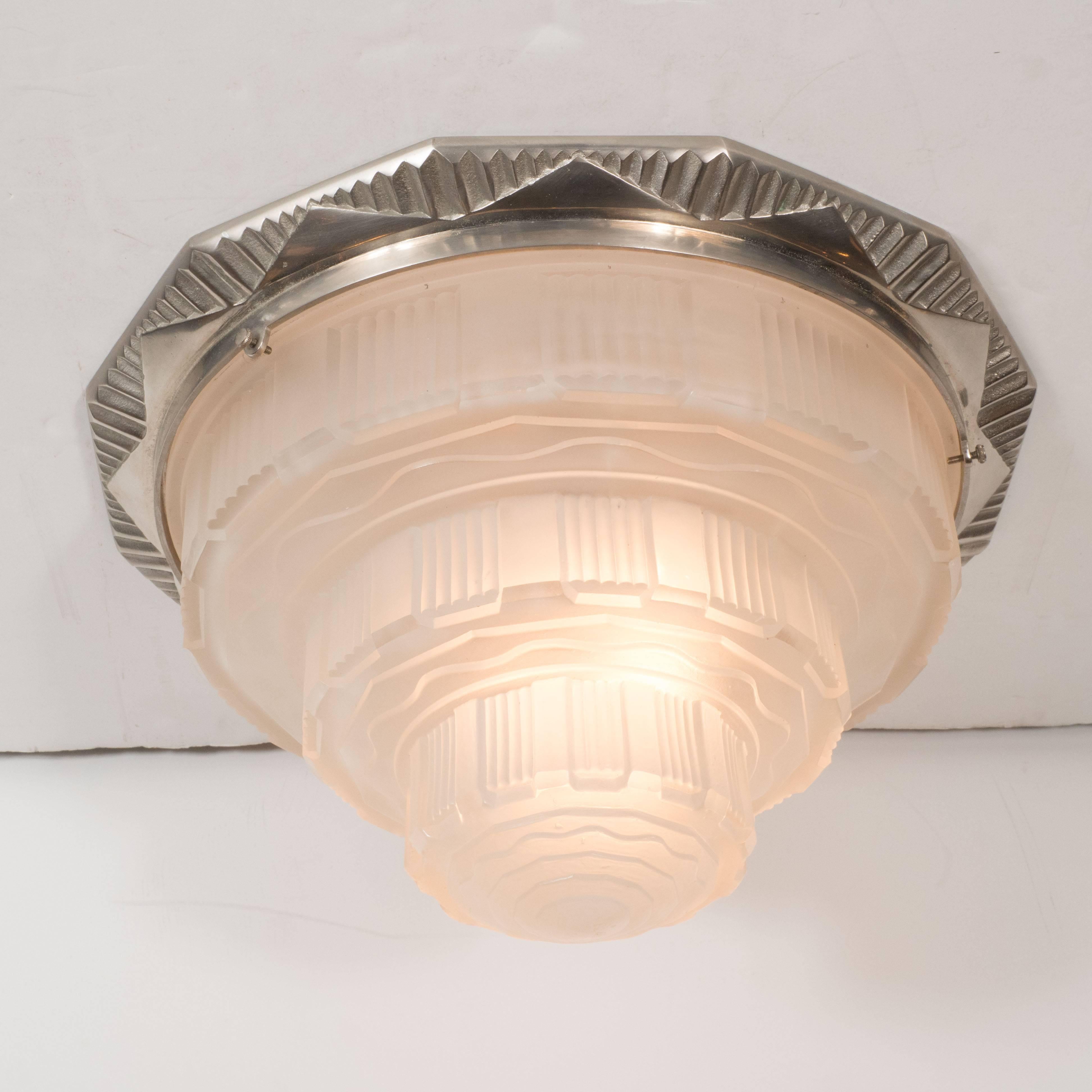 This elegant skyscraper style flush mount was realized in France, circa 1930 by the celebrated atelier Gênet et Michon. It features a nickel plated bronze base with sunburst striations and pyramidal geometric forms circumscribing the perimeter.