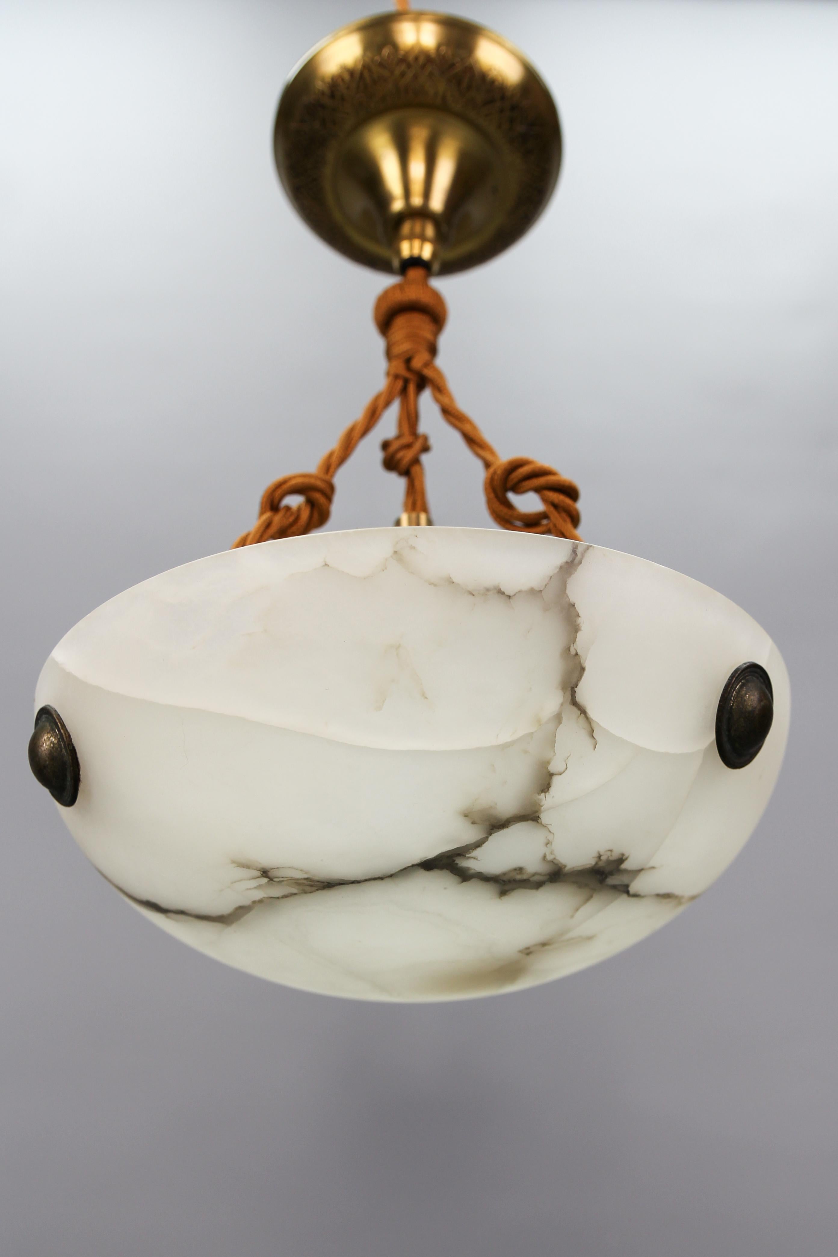 French Art Deco white and black veined alabaster pendant light fixture.
A small and adorable alabaster pendant ceiling light fixture from circa the 1930s. The beautifully veined white alabaster bowl is suspended by three ropes (wires) and a brass