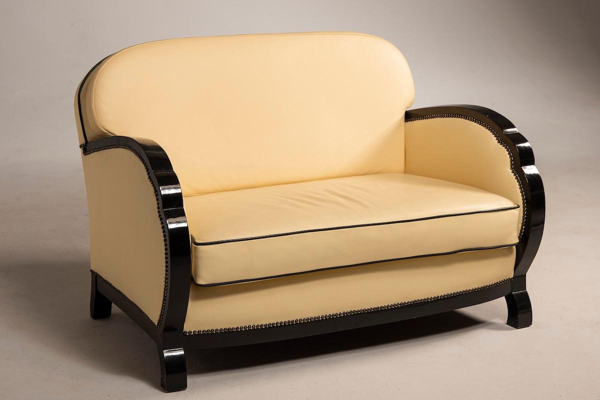 The entire ensemble features elegant black leather details contrasted by ivory-colored leather upholstery. One of the armchairs in the set is reclining, while the second and the sofa both have fixed backs. The cushions have been newly crafted, while